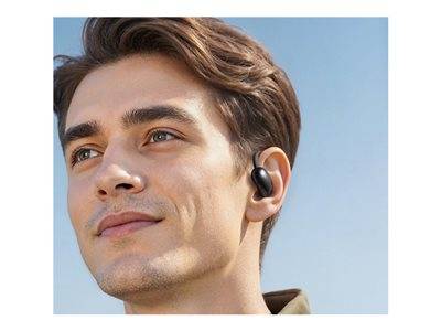 Eine Person mit kurzen Haaren, die schwarze kabellose Kopfhörer trägt, schaut mit einem neutralen Gesichtsausdruck nach oben. Der Himmel ist im Hintergrund sichtbar.