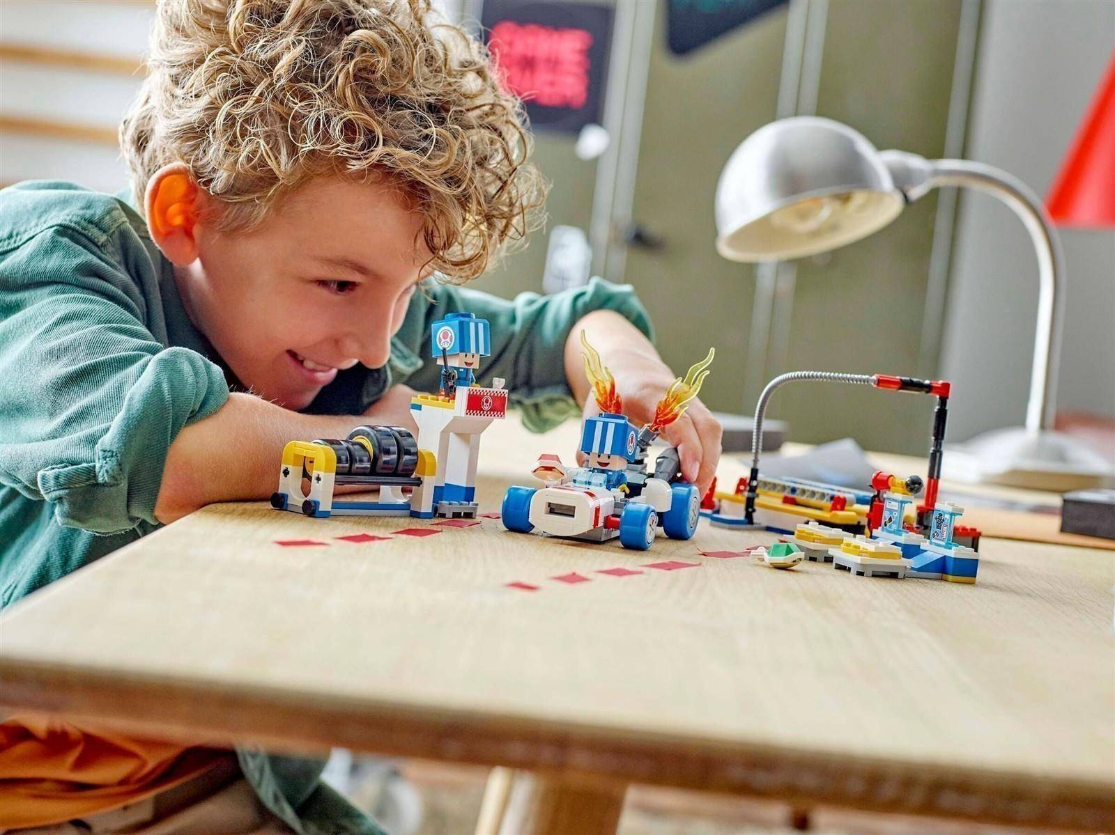 Kind mit lockigem Haar, das mit einem LEGO-ähnlichen Roboter und Teilen auf einem Tisch spielt, konzentriert sich darauf, ein kleines Spielzeug-Setup in einem Wohnzimmer zu bauen.