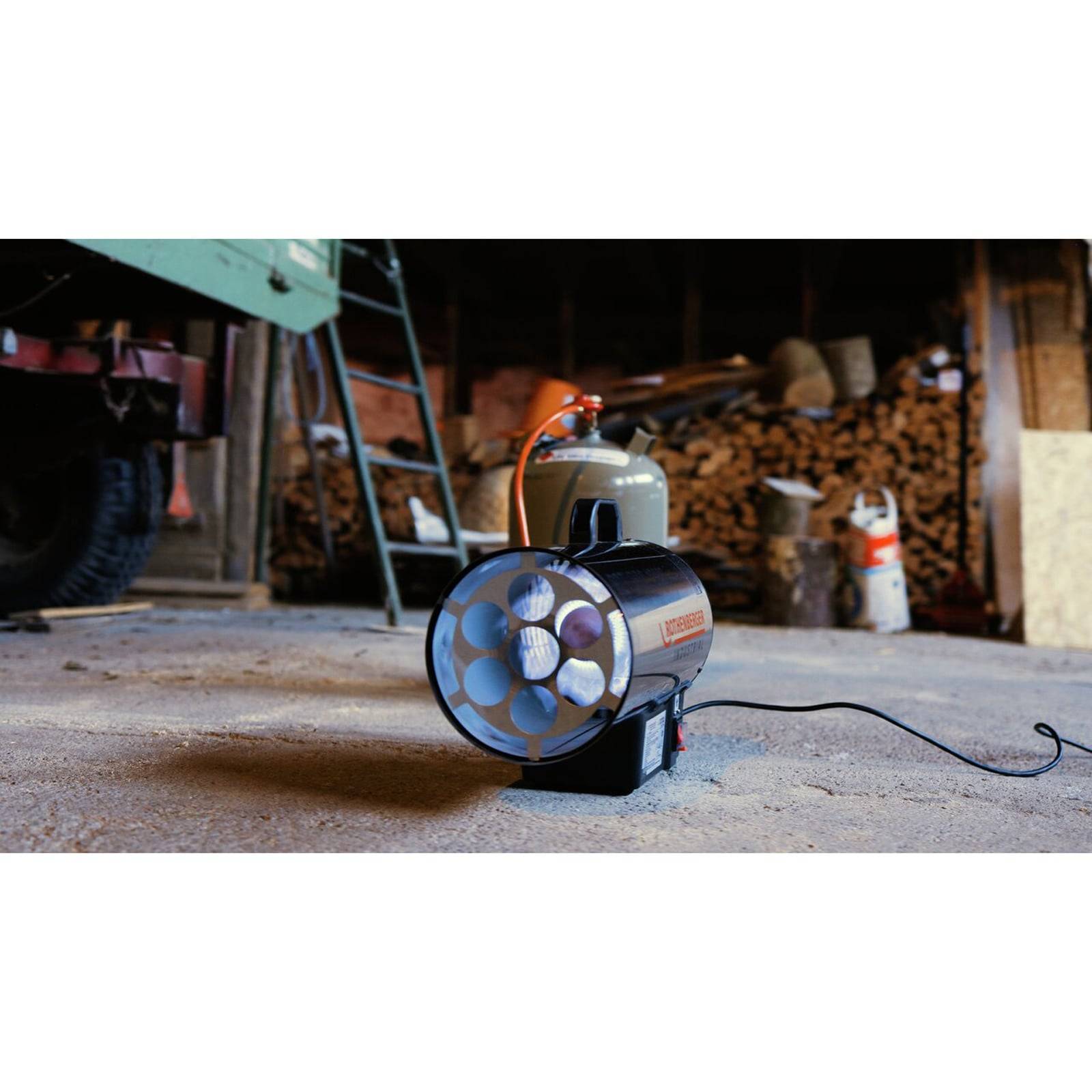 Tragbarer Propangasofen auf einem Werkstattboden mit einem Holzstapel und Werkzeugen im Hintergrund, der seinen Einsatz in Baustellenumgebungen veranschaulicht.