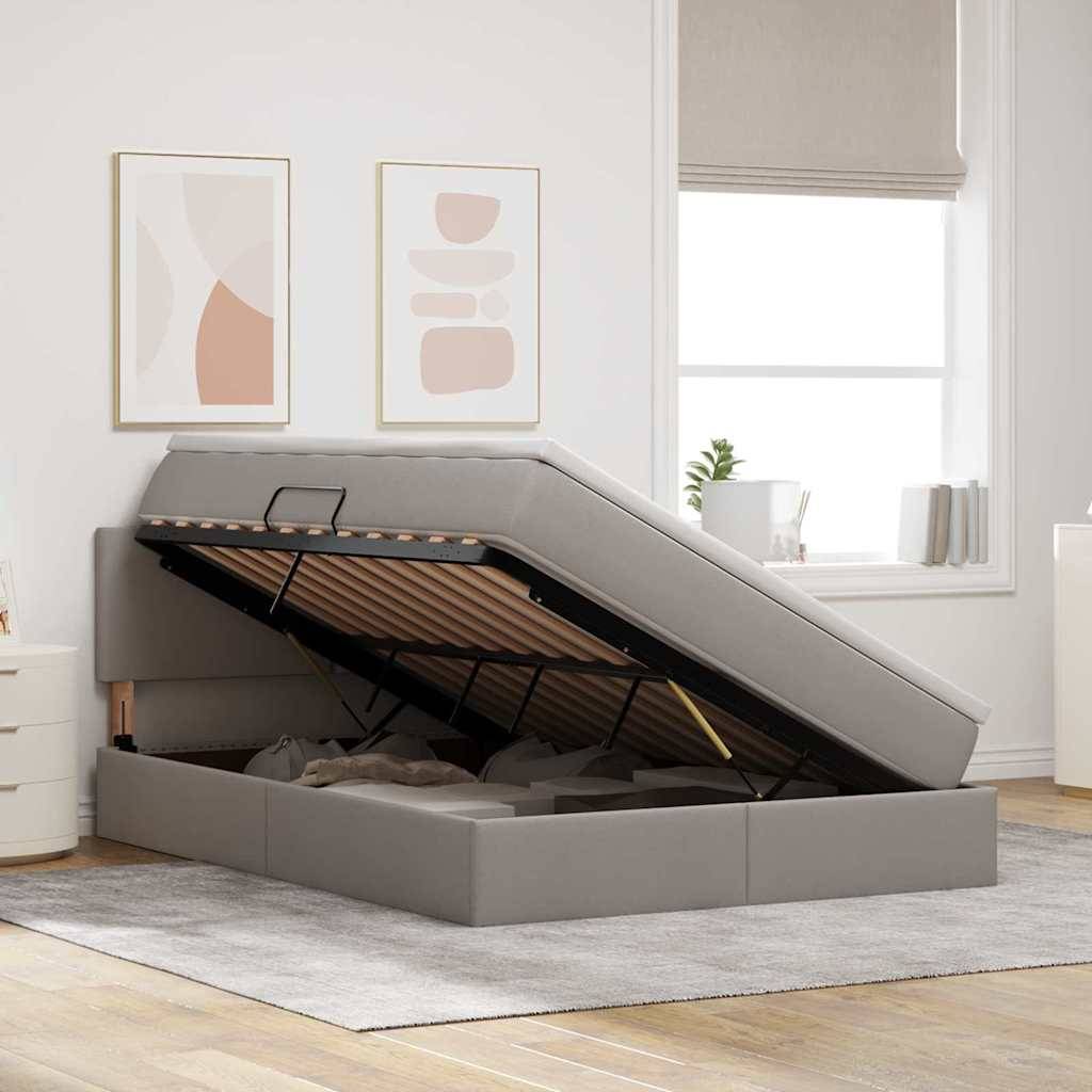 Ein Schlafzimmer mit einem offenen grauen Speicherbett, das Stauraum enthüllt, auf einem hellen Teppich. Zwei abstrakte gerahmte Kunstwerke und eine Pflanze befinden sich im Hintergrund.