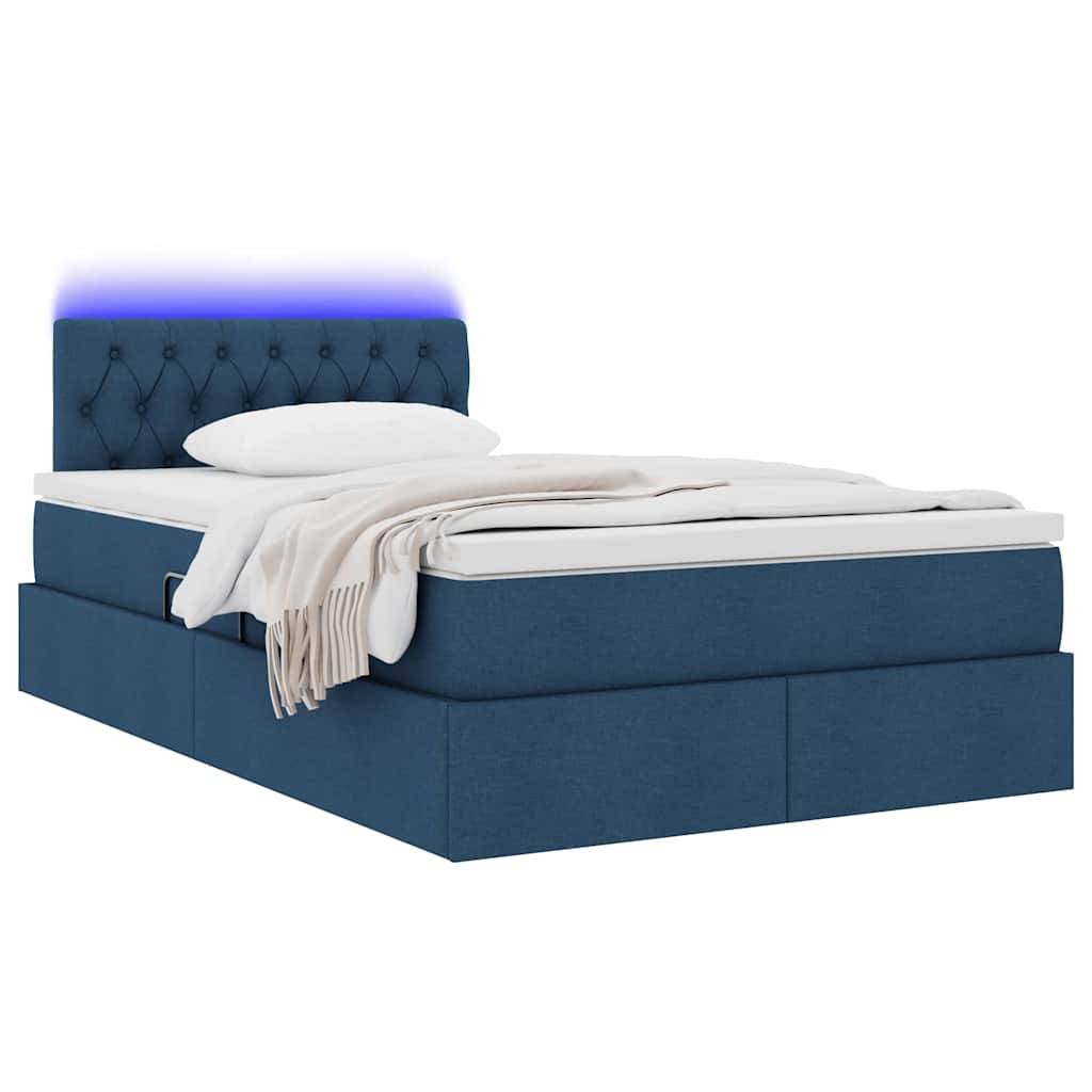 Ein Bett mit blauem Polsterstoff, gestepptem Kopfteil, Schubladen zur Unterbettlagerung, weißer Bettwäsche und einer Decke. LED-Leuchten verbreiten ein blaues Licht.