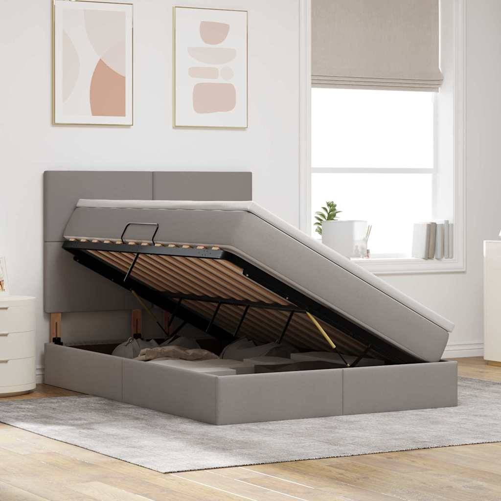 Ein modernes Schlafzimmer mit einem grau gepolsterten Bett, das einen offenen Stauraum unter der Matratze aufweist. Weiße Wände und ein großes Fenster.