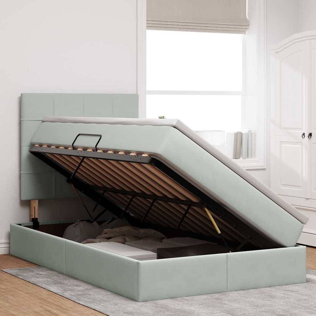 Ein modernes Schlafzimmer zeigt ein hellgraues Bett mit Stauraum, wobei die Matratze angehoben ist und den Stauraum darunter offenlegt. Ein großes Fenster sorgt für natürliches Licht.