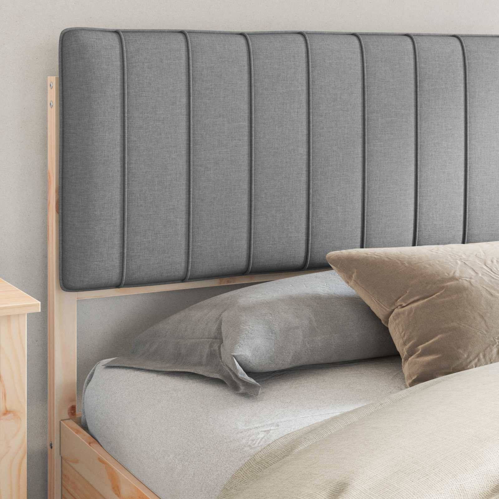Bett mit einer grauen, gepolsterten Kopfseite und passenden Kissen, vor einer hellgefärbten Wand. Minimalistischer Holzrahmen.