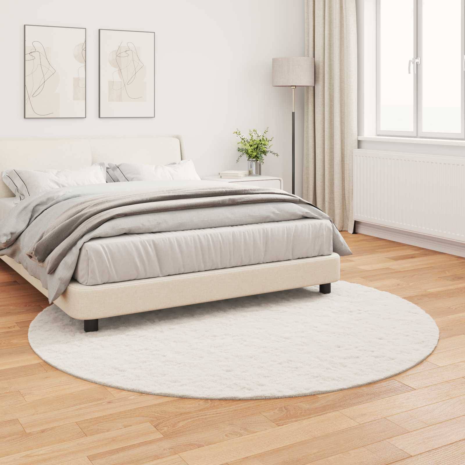 Ein ordentlich gemachtes Bett in einem modernen Schlafzimmer mit hellgefärbter Bettwäsche, zwei gerahmte abstrakte Kunstwerke darüber und ein runder Teppich auf Holzboden.