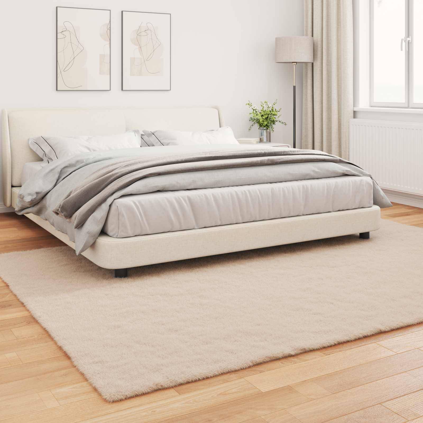 Ein modernes Schlafzimmer mit einem beigen Bett, weiß-grauer Bettwäsche, einer Stehlampe, zwei einfachen Strichzeichnungen an der Wand und einem großen Fenster.