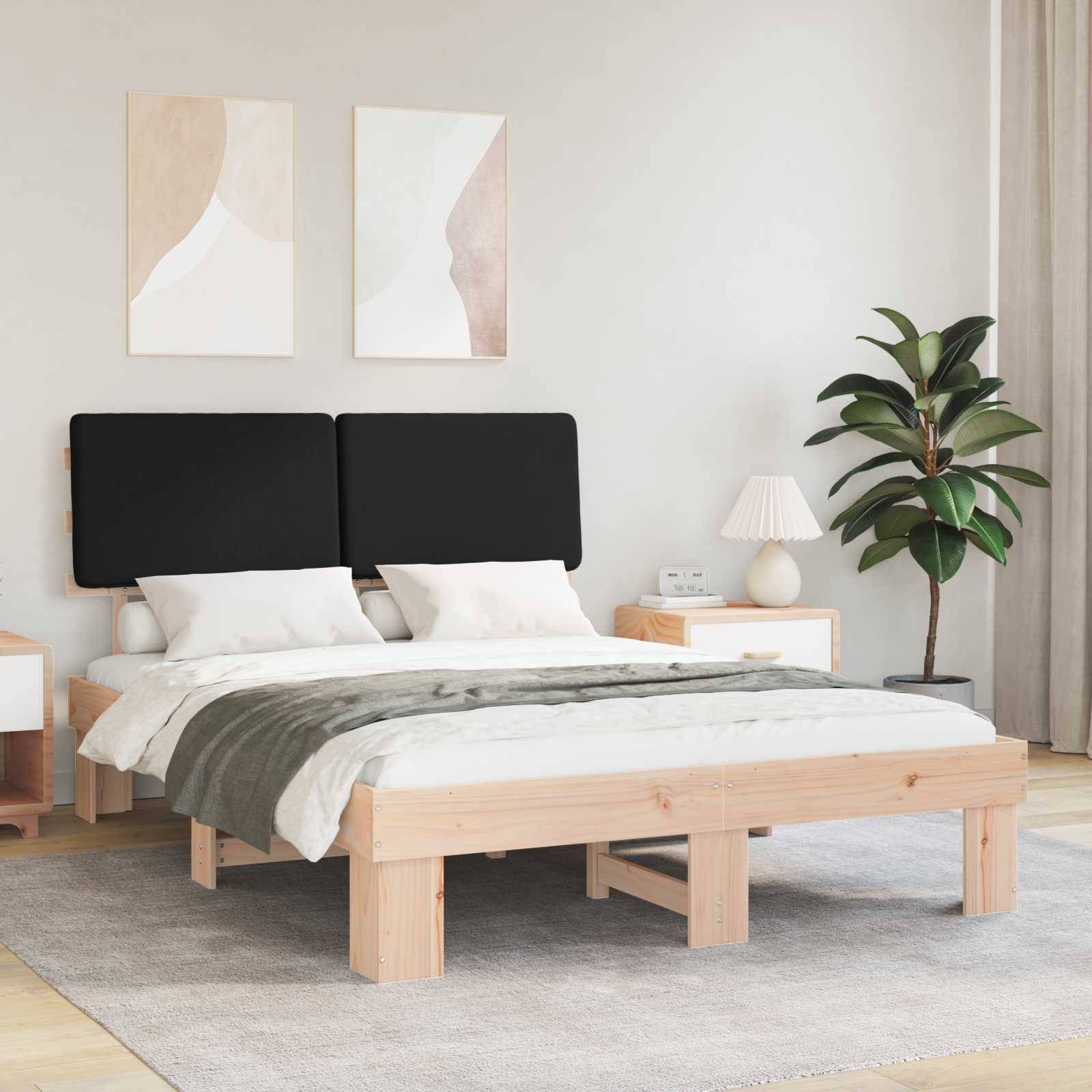 Ein modernes Schlafzimmer zeigt ein Holzbett mit schwarzen Kissen, weiß-grauer Bettwäsche, Nachttischen, einer Lampe und einer Zimmerpflanze.