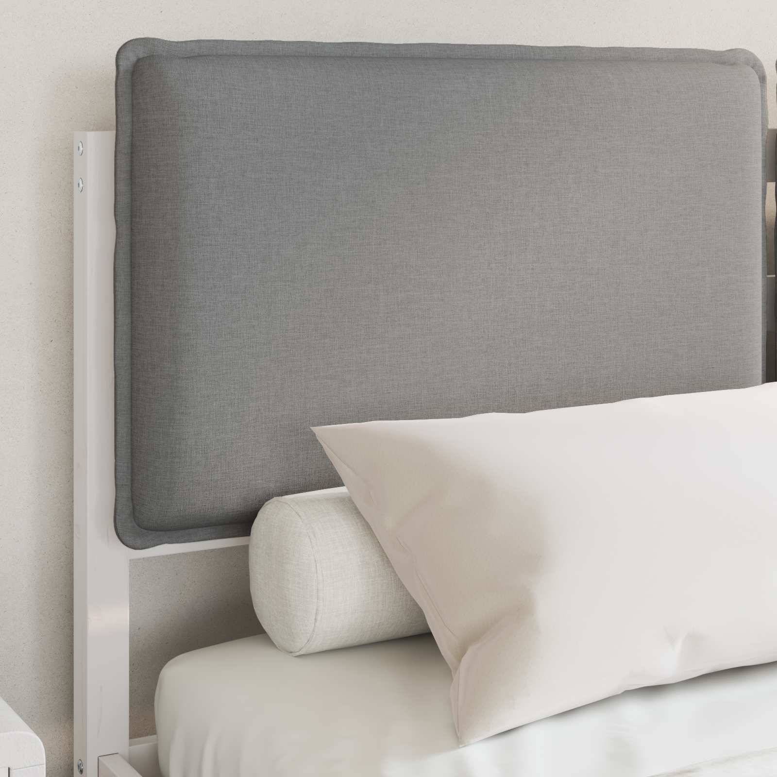 Ein Bett mit einem grauen gepolsterten Kopfteil, weißer Bettwäsche und einem zylindrischen Kissen, vor einer hellgefärbten Wand.