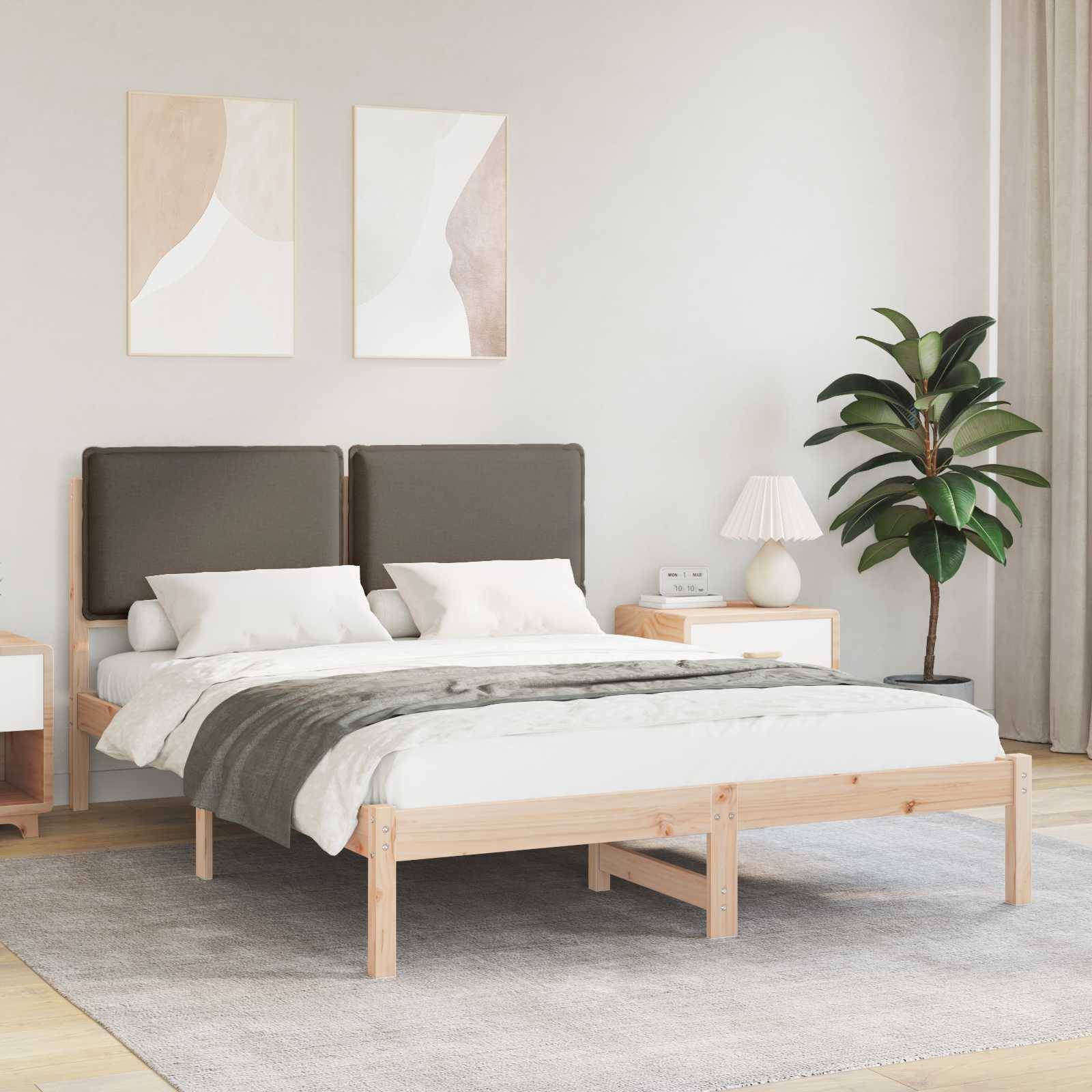 Ein modernes Schlafzimmer mit einem Holzbett, grauer Bettwäsche, zwei abstrakten Kunstwerken über dem Kopfteil, einer Topfpflanze und einem Nachttisch mit einer Lampe.