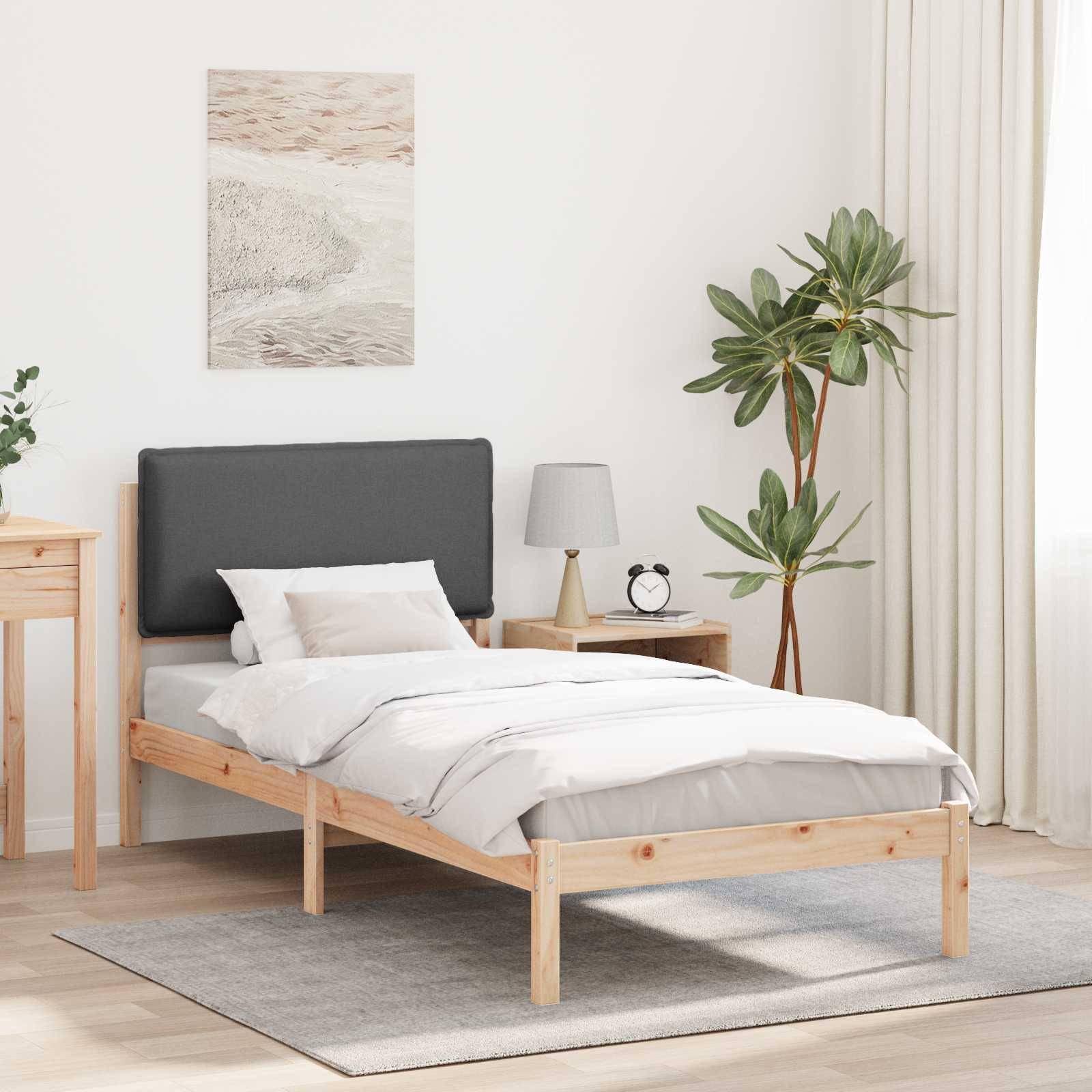Ein minimalistisches Schlafzimmer mit einem Holzbett mit grauem Kopfteil, weißer Bettwäsche, einem Nachttisch mit Lampe, einer Topfpflanze und Kunstwerken an der Wand.