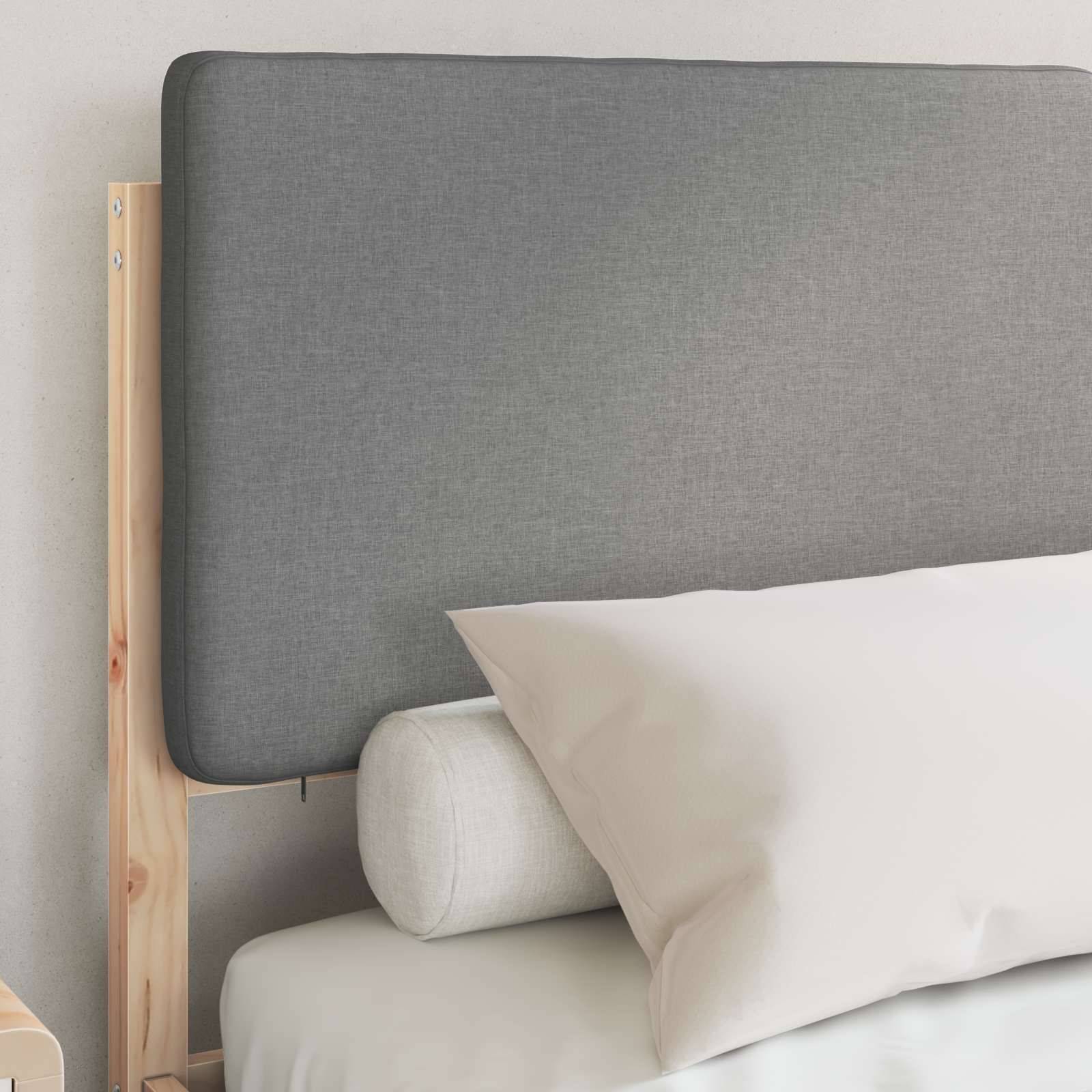 Ein ordentlich gemachtes Bett mit einem hellgrauen gepolsterten Kopfteil, Holzrahmen und weißem Kissen, das einen klaren und modernen Eindruck vermittelt.