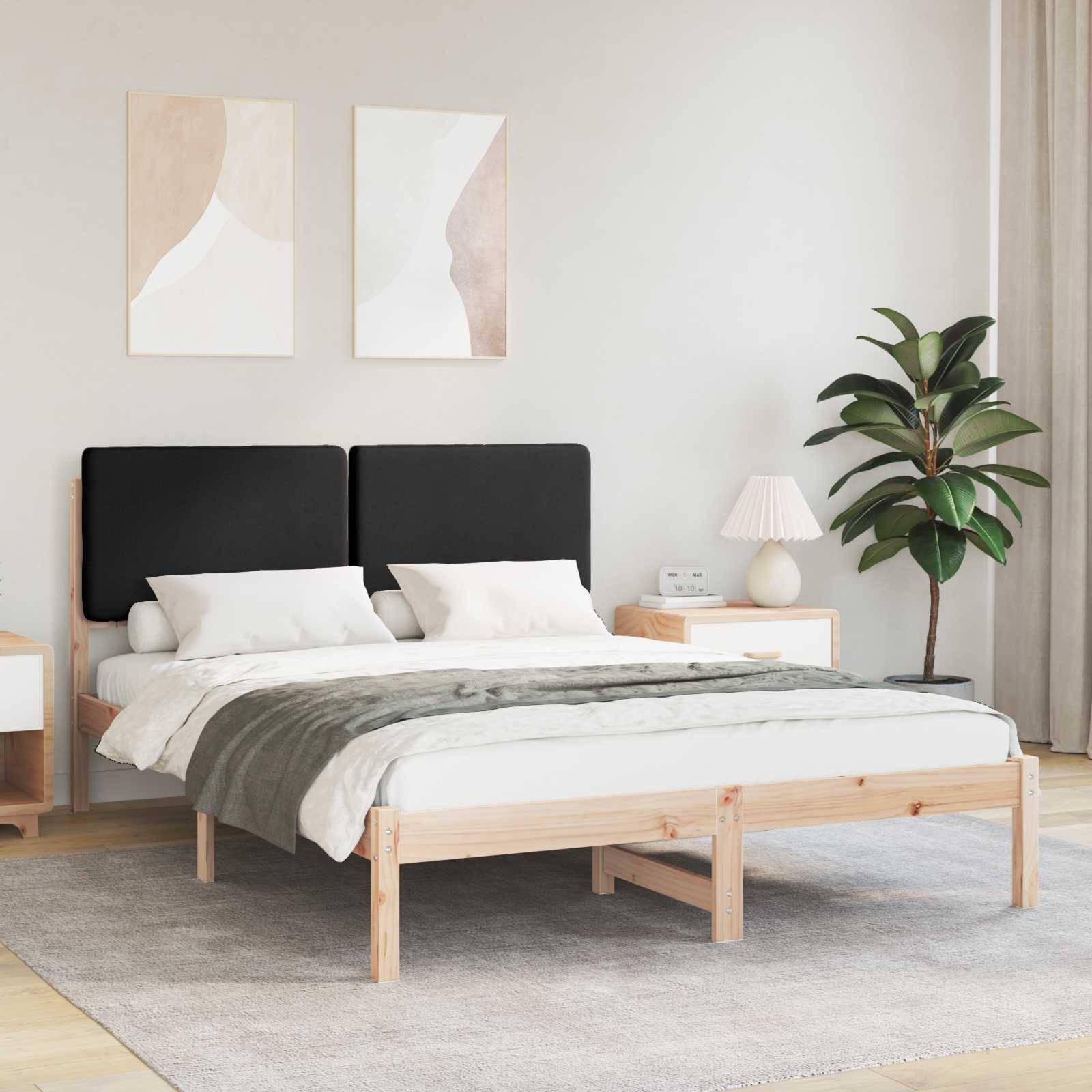 Ein modernes Schlafzimmer mit einem Holzbett, schwarzem Kopfteil und weißer Bettwäsche. Eine Lampe, eine Pflanze und abstrakte Kunst verleihen dekorative Akzente.