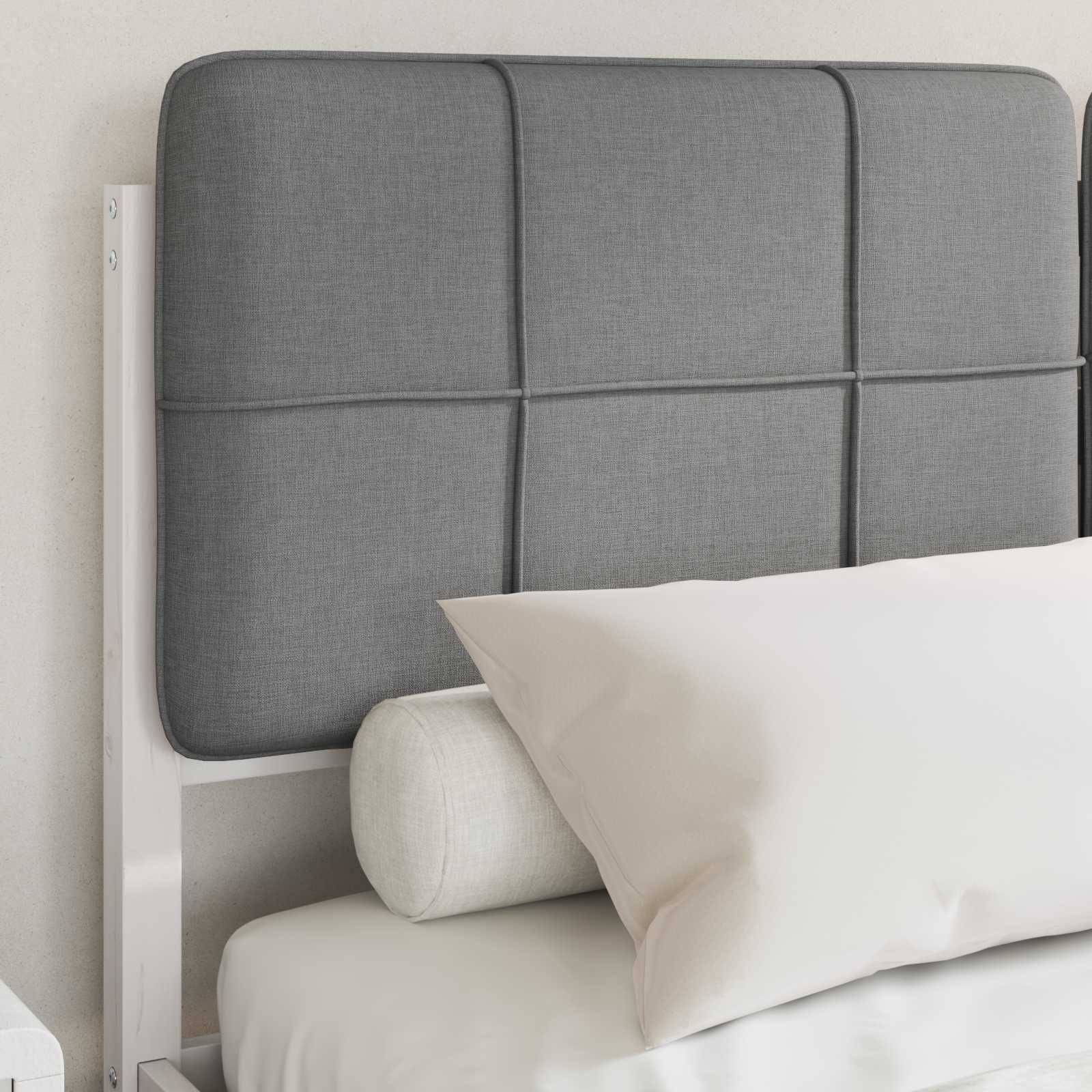 Ein ordentlich gemachtes Bett mit einem weißen Kissen, einem grauen gepolsterten Kopfteil und einem kleinen zylindrischen Stützkissen vor einer neutralen Wand.