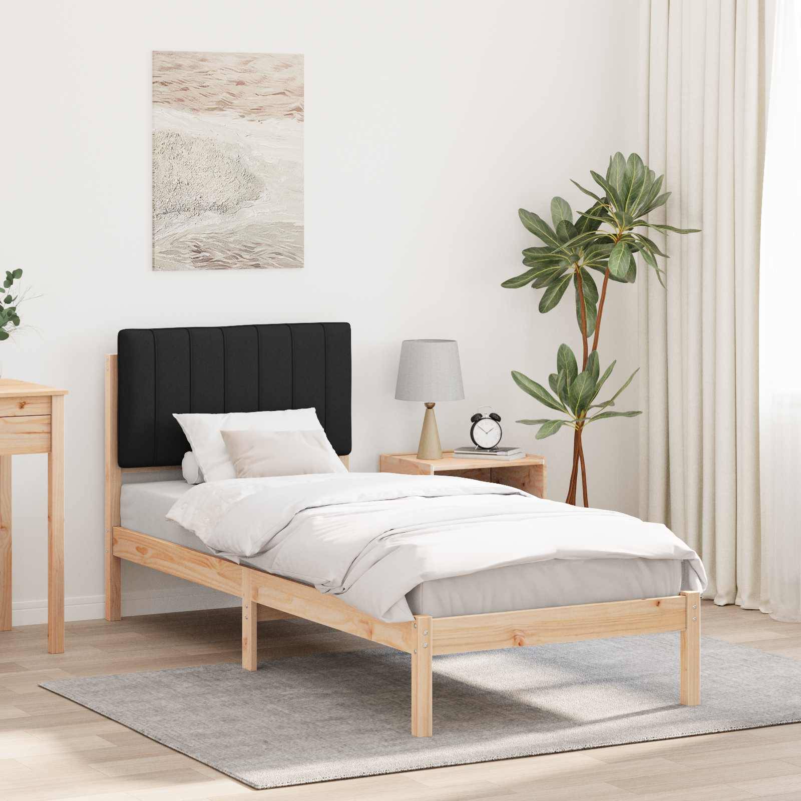 Ein minimalistisches Schlafzimmer mit einem Einzelbett mit schwarzem Kopfteil, weißer Bettwäsche und Holzrahmen. Ein Nachttisch mit einer Lampe. Eine Pflanze und ein gerahmtes Kunstwerk verleihen dem Raum Dekoration.