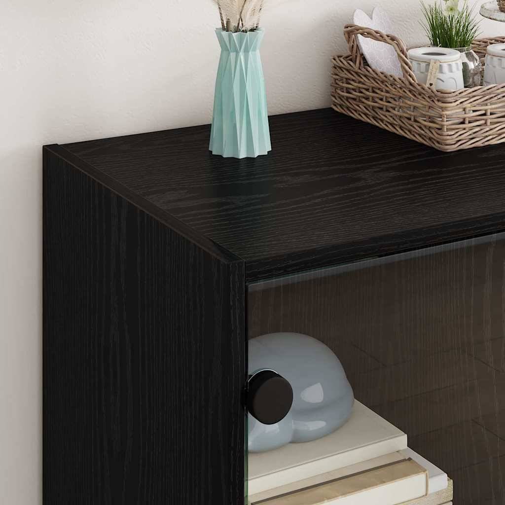 Ein schwarzer Holzschrank mit einer glatten Vase, in der eine Pflanze steht, und einem Flechtkorb oben darauf, nahe einer Wand. Ordentlich aufgereihte Bücher auf dem unteren Regal sichtbar.