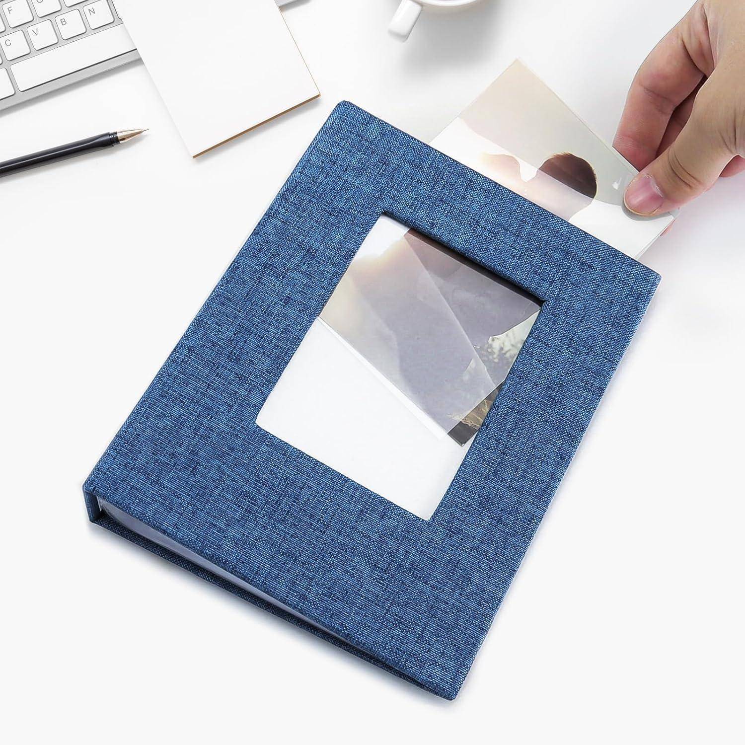 Eine Hand legt ein Foto in ein blaues Fotoalbum auf einem Schreibtisch. In der Nähe befinden sich ein Bleistift, eine Tasse und Papiere, was auf eine persönliche Organisations- oder Gedächtnisbewahrungsaktivität hindeutet.