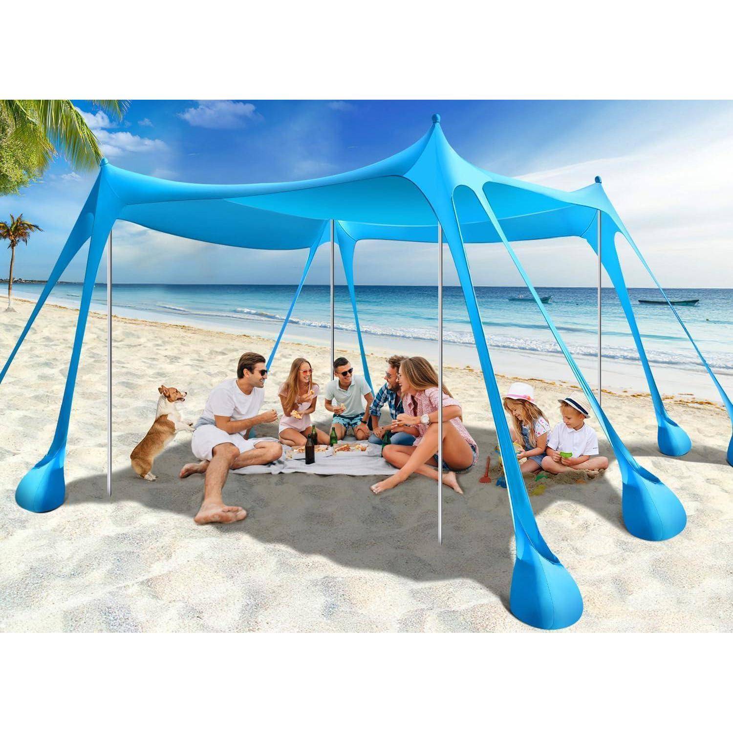 Eine Gruppe von Menschen unter einem blauen Sonnenschirm am Strand. Sie sitzen auf dem Sand, unterhalten sich und genießen einen sonnigen Tag. Ein Hund ist in der Nähe.