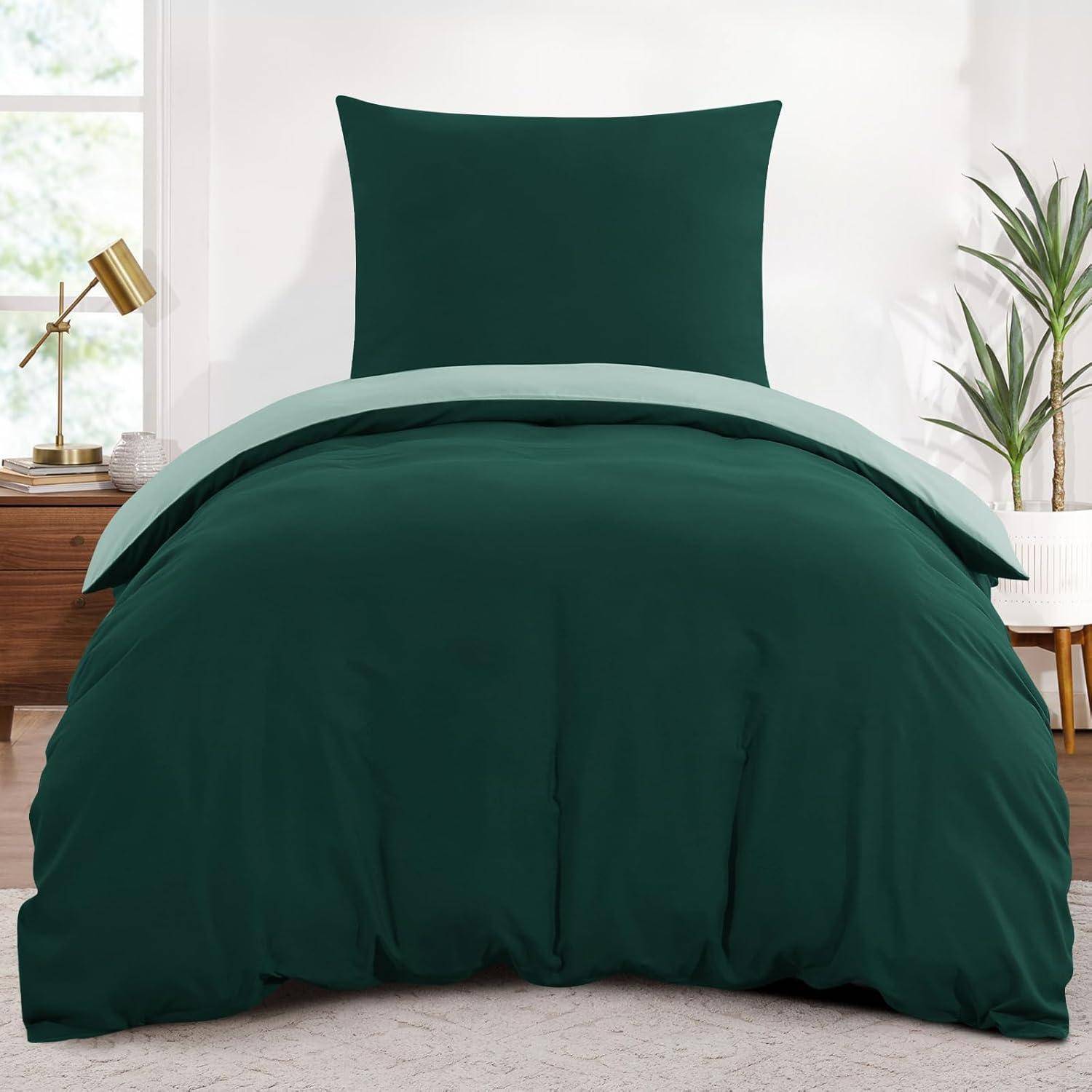 Ein Schlafzimmer mit einem Bett, das mit einer dunkelgrünen Bettdecke und Kissen bezogen ist, neben einem kleinen Holztisch mit einer Lampe und einer Pflanze darauf.