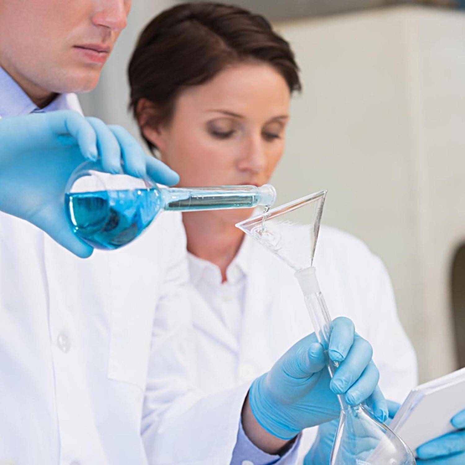 Zwei Wissenschaftler in Laborkitteln und Handschuhen führen ein Experiment mit einer blauen Flüssigkeit durch, wobei sie sich auf einen Kolben und einen Trichter in einer Laborumgebung konzentrieren.