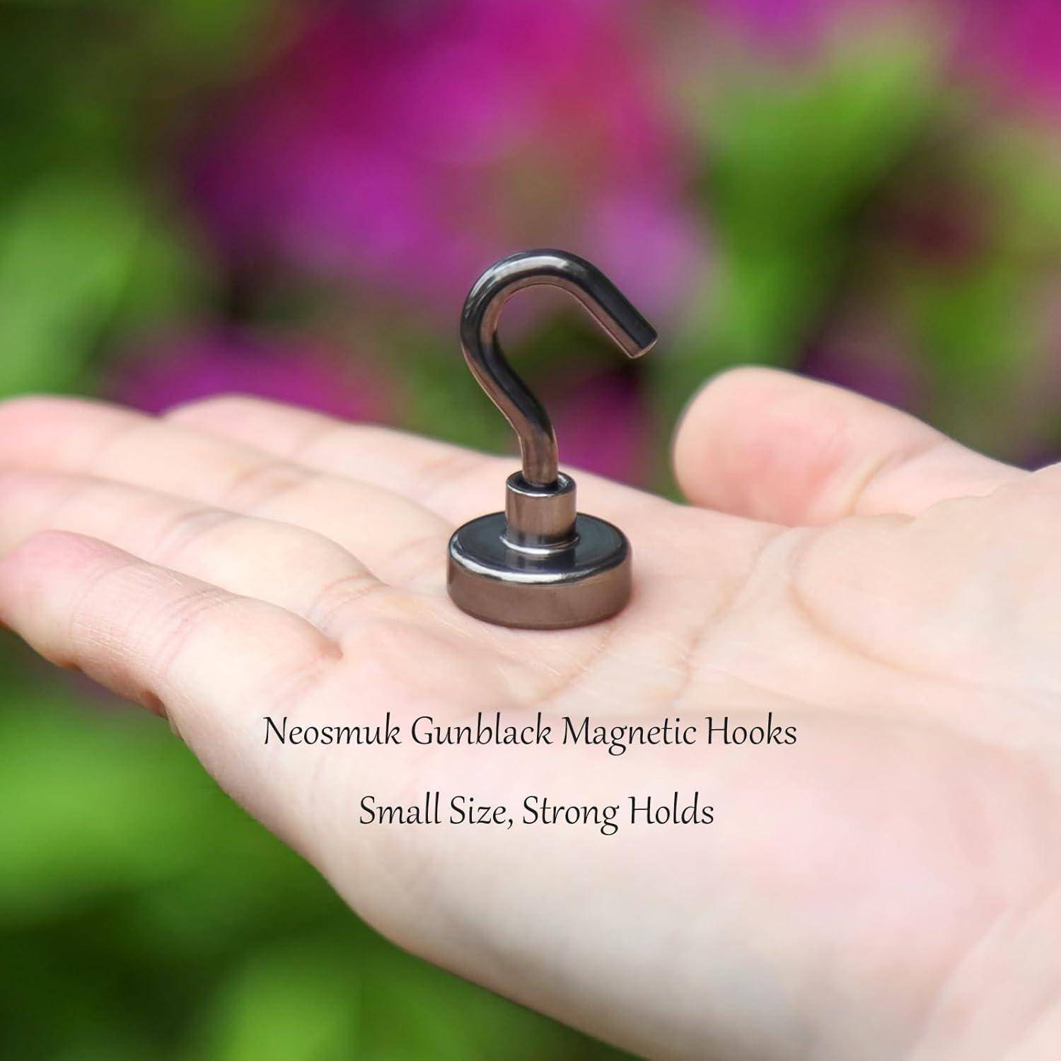 Eine Hand hält einen kleinen magnetischen Haken von Neosmuk. Der Text lautet: 'Neosmuk Gunblack Magnetische Haken: Kleine Größe, Starke Halterung'.