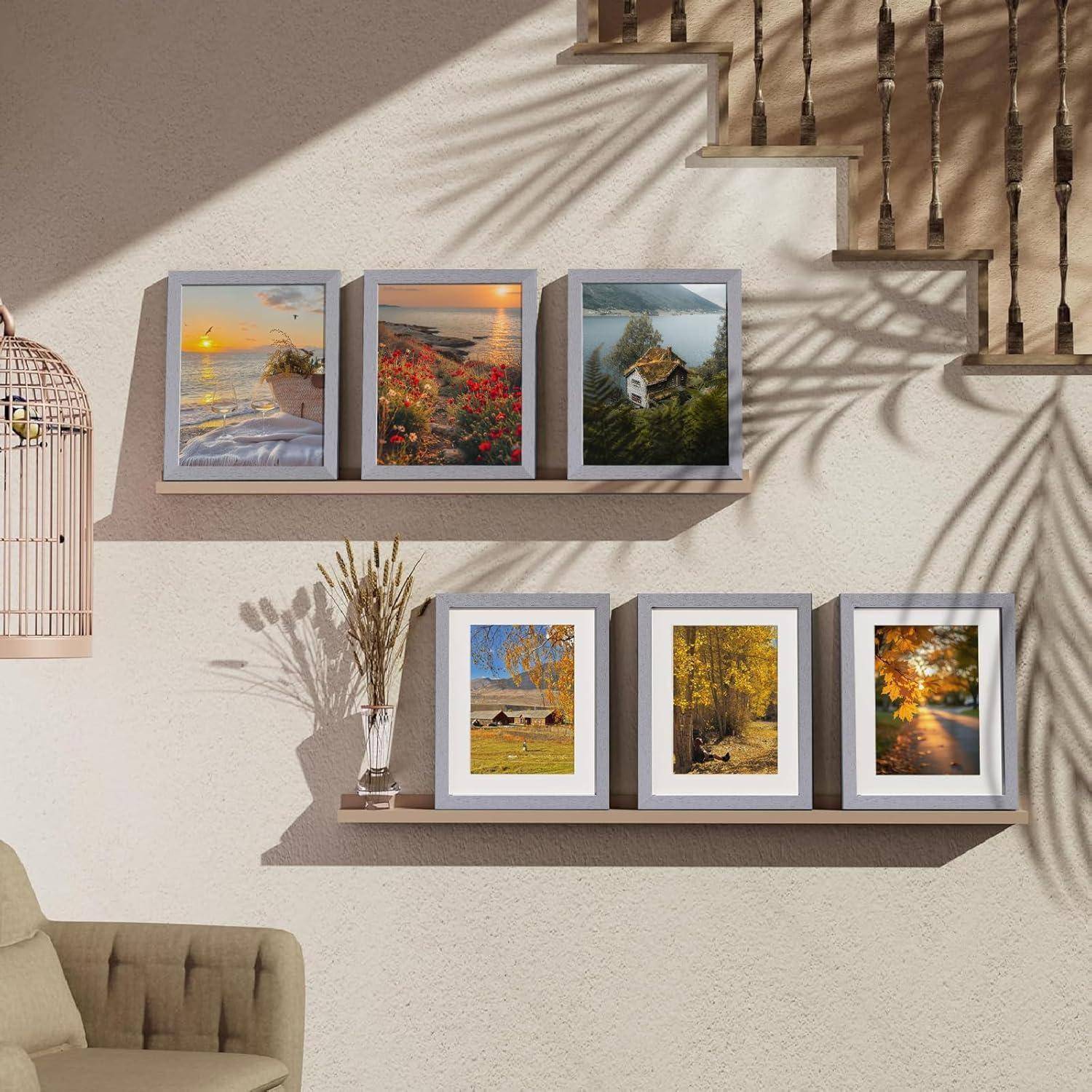 Ein gut beleuchteter Wohnzimmerbereich mit einer Wand, auf der sechs gerahmte Landschaftsfotos auf zwei Regalen angeordnet sind; die Treppe wirft Schatten an die Wand.