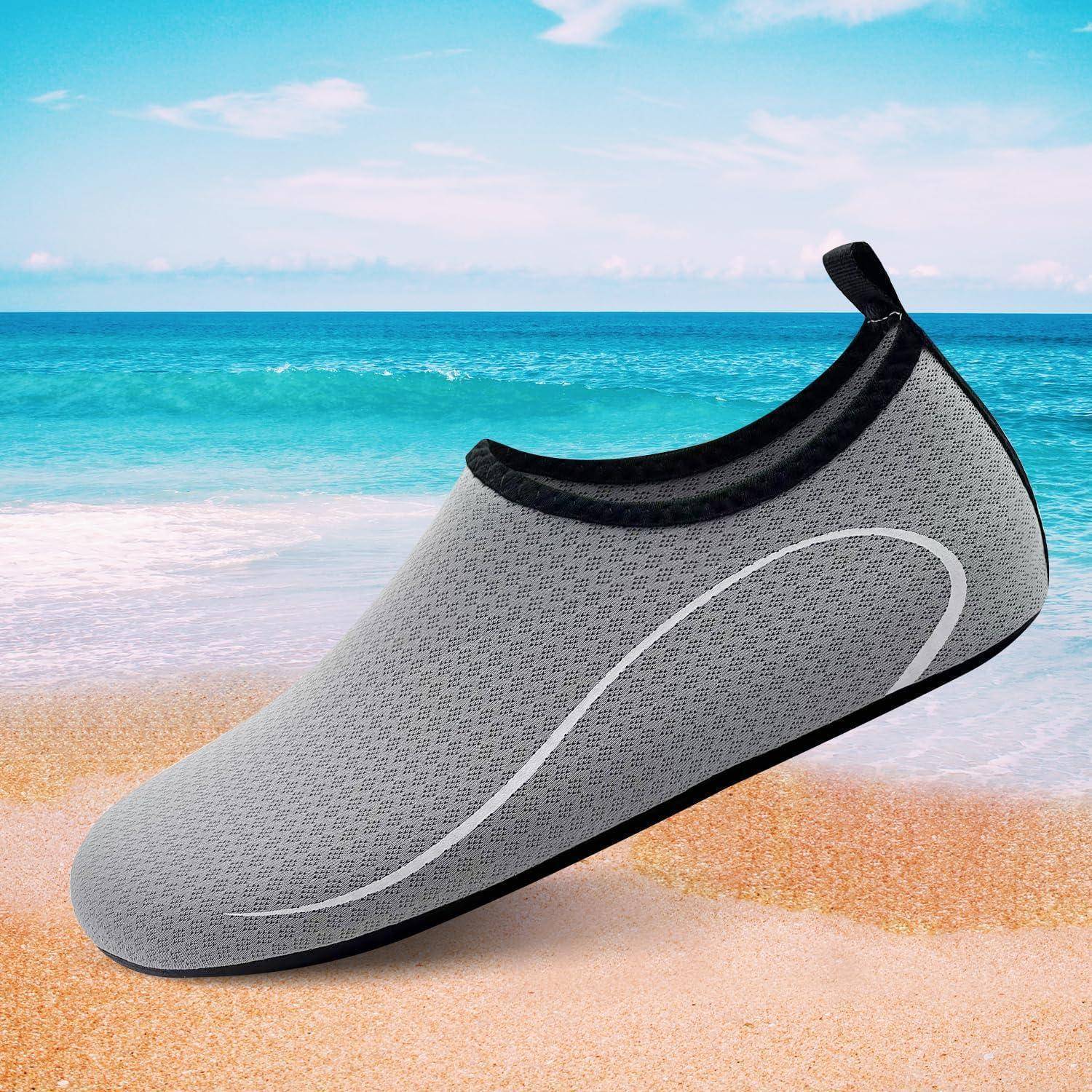 Ein Grau-Wasserschuh mit schwarzem Rand wird an einem sandigen Strand am Ozean präsentiert, was seine Eignung für Strand-Aktivitäten unterstreicht.