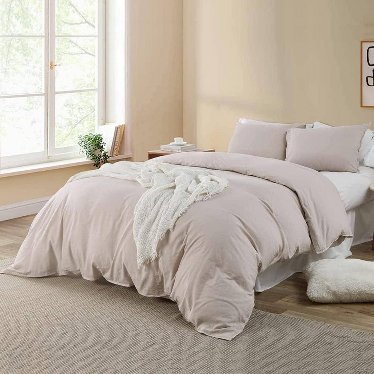 Ein gemütliches Schlafzimmer mit einem großen Bett, das mit weicher, blassrosa Bettwäsche, einer leichten Decke und zwei Kissen ausgestattet ist. Ein Fenster lässt natürliches Licht herein.
