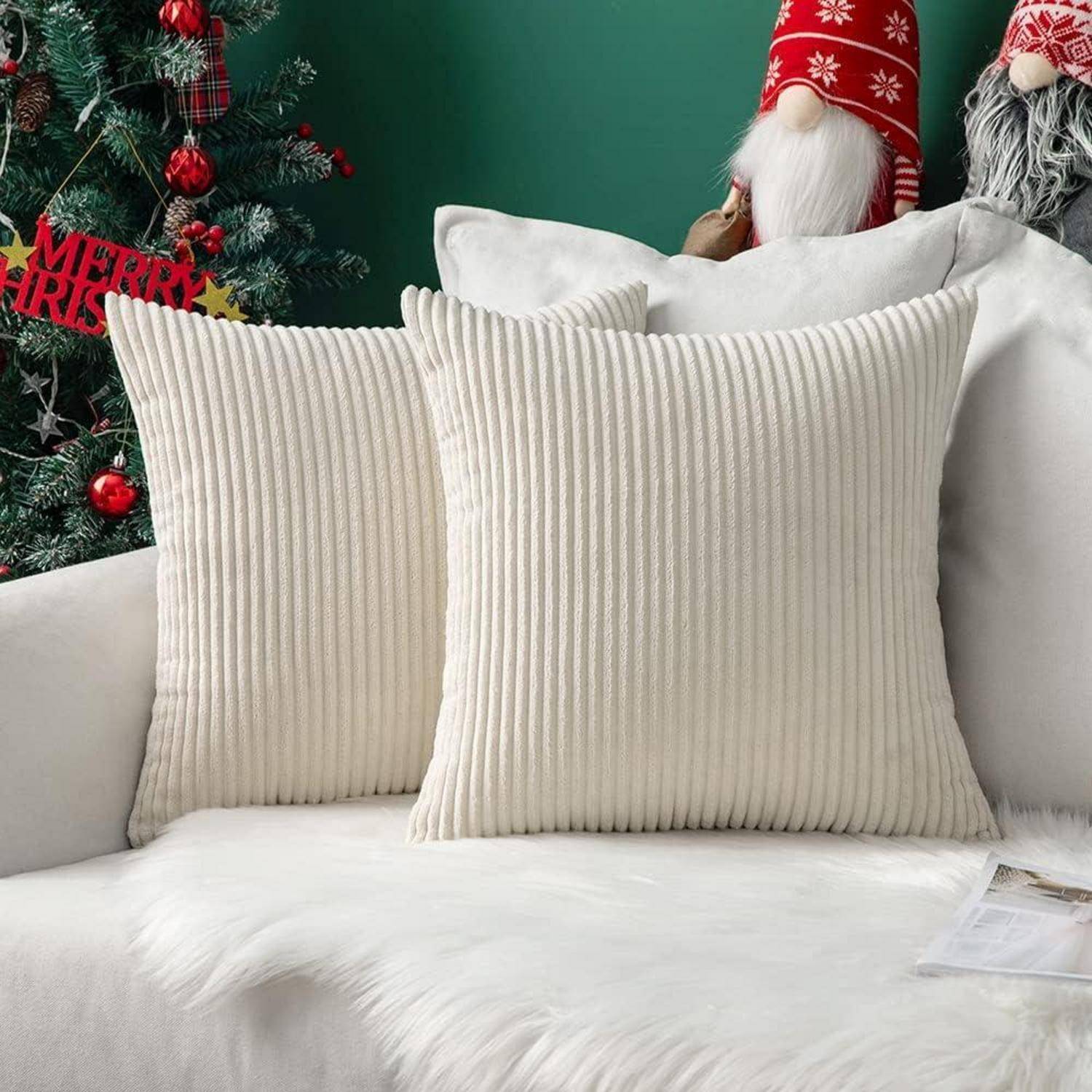 Zwei beige Kissen auf einem weißen Sofa vor einer grünen Wandkulisse. Eine plüschige Weihnachtsmannfigur und rote Weihnachtsdekoration verleihen dem Raum eine festliche Atmosphäre.