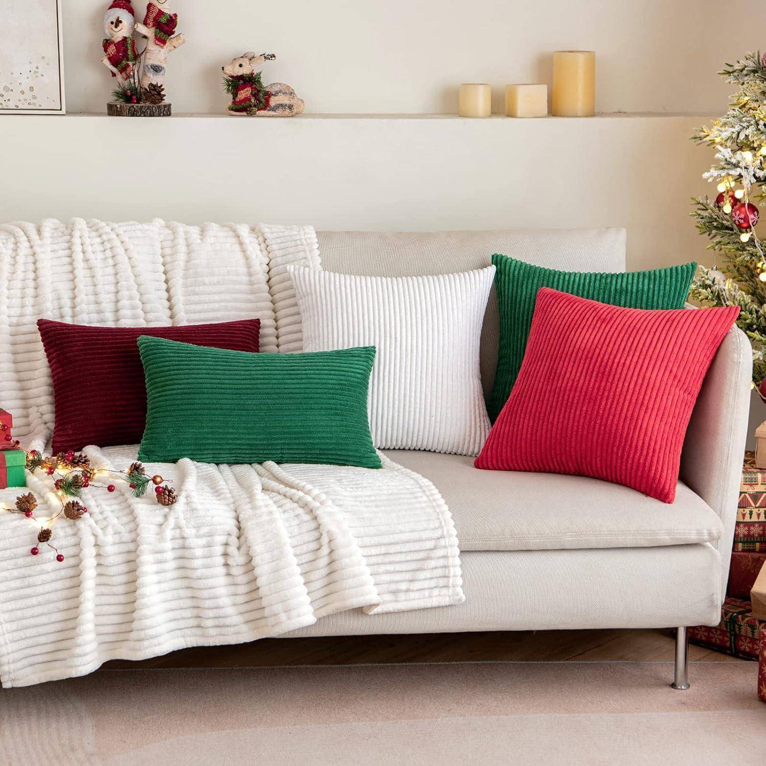 Ein gemütliches Wohnzimmer mit einem weißen Sofa, geschmückt mit roten, grünen und weißen Kissen. Festliche Dekorationen und eine kleine Weihnachtsmann-Figur sind zu sehen.