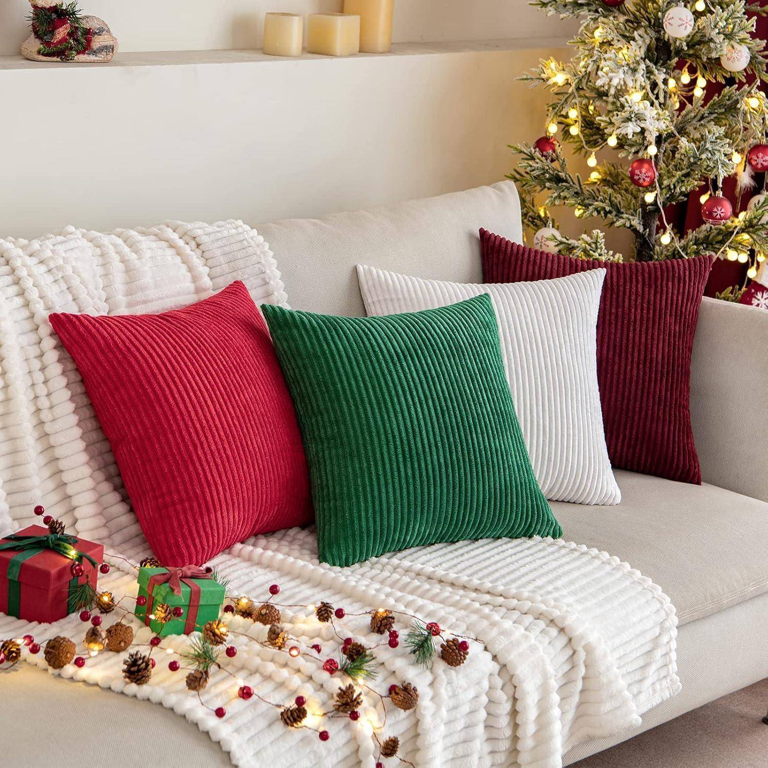 Ein gemütliches Wohnzimmer mit einem Sofa, das mit roten, grünen und weißen Kissen geschmückt ist, begleitet von Weihnachtsdekoration und einem geschmückten Weihnachtsbaum.
