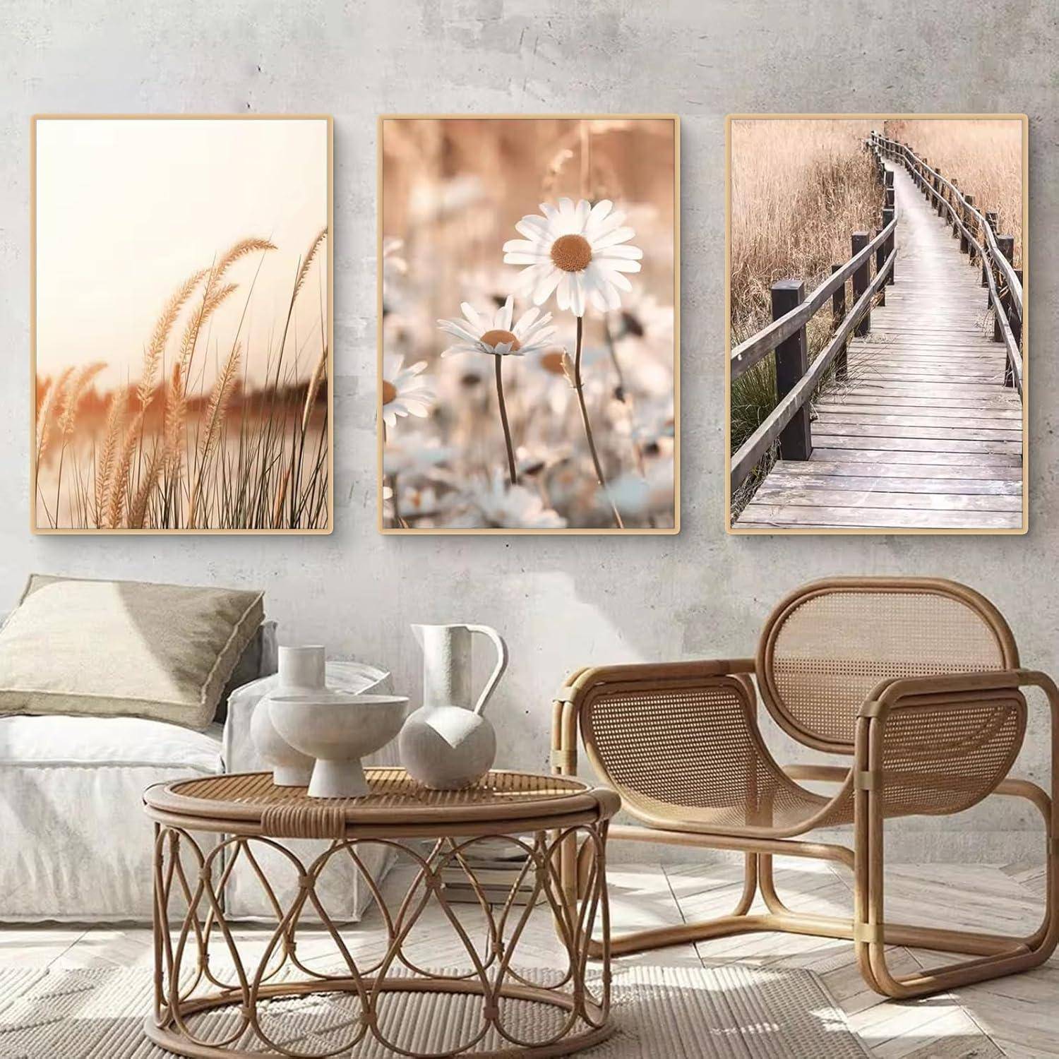 Ein gemütliches Wohnzimmer mit einem weißen Sofa und Rattanstühlen. Drei gerahmte Naturfotos an der Wand zeigen Gräser, Gänseblümchen und einen Steg.