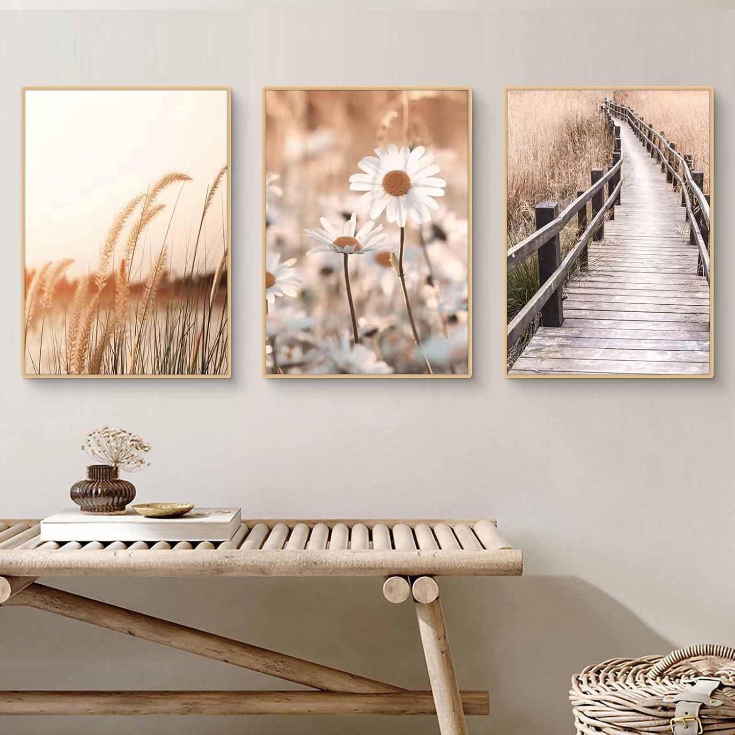 Eine Wand mit drei gerahmten naturthematischen Fotografien: Weizenfeld, Gänseblümchen, Holzsteg. Darunter eine Holzbank mit Büchern und Dekoration.