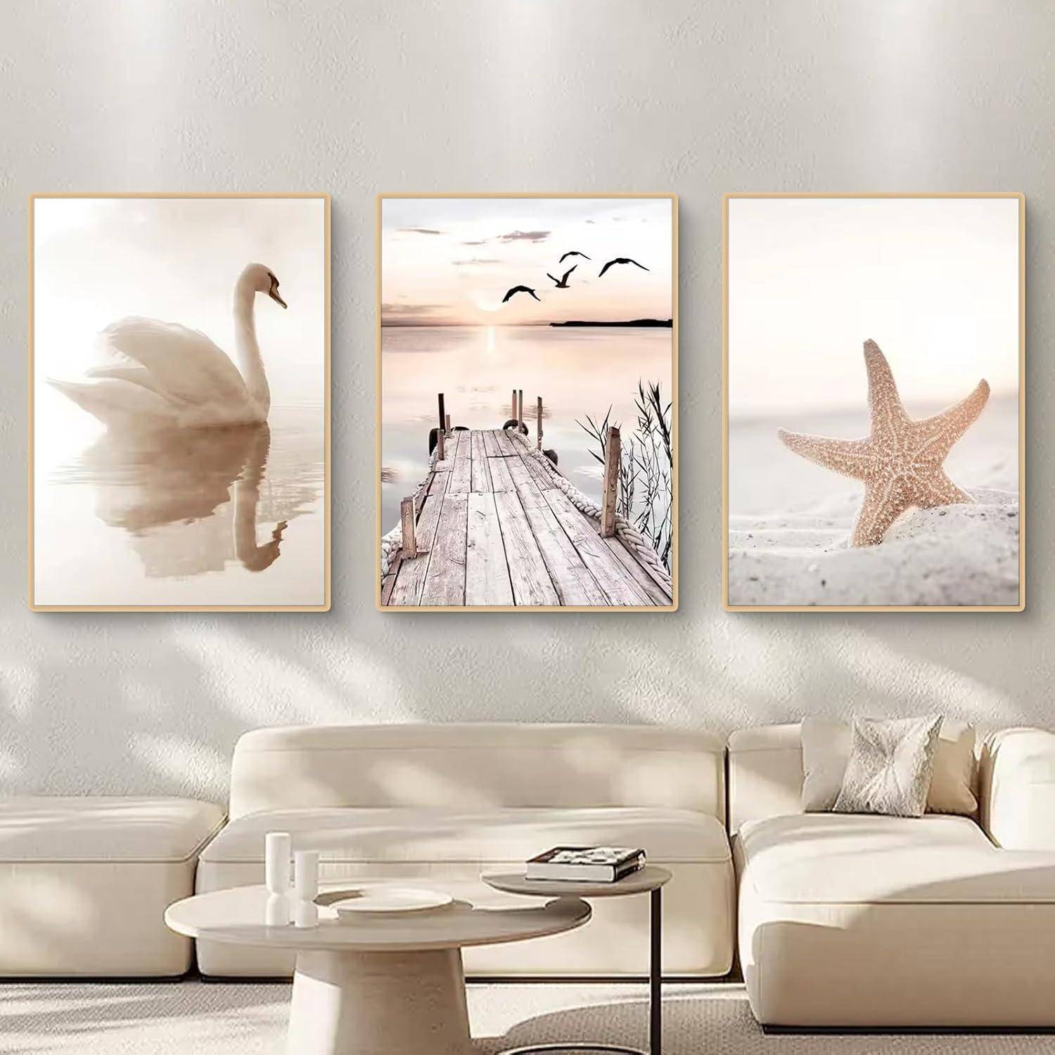 Drei gerahmte Kunstwerke an einer Wand über einem weißen Sofa. Die Bilder zeigen einen Schwan auf Wasser, einen Holzsteg mit fliegenden Vögeln und einen Seestern auf Sand.