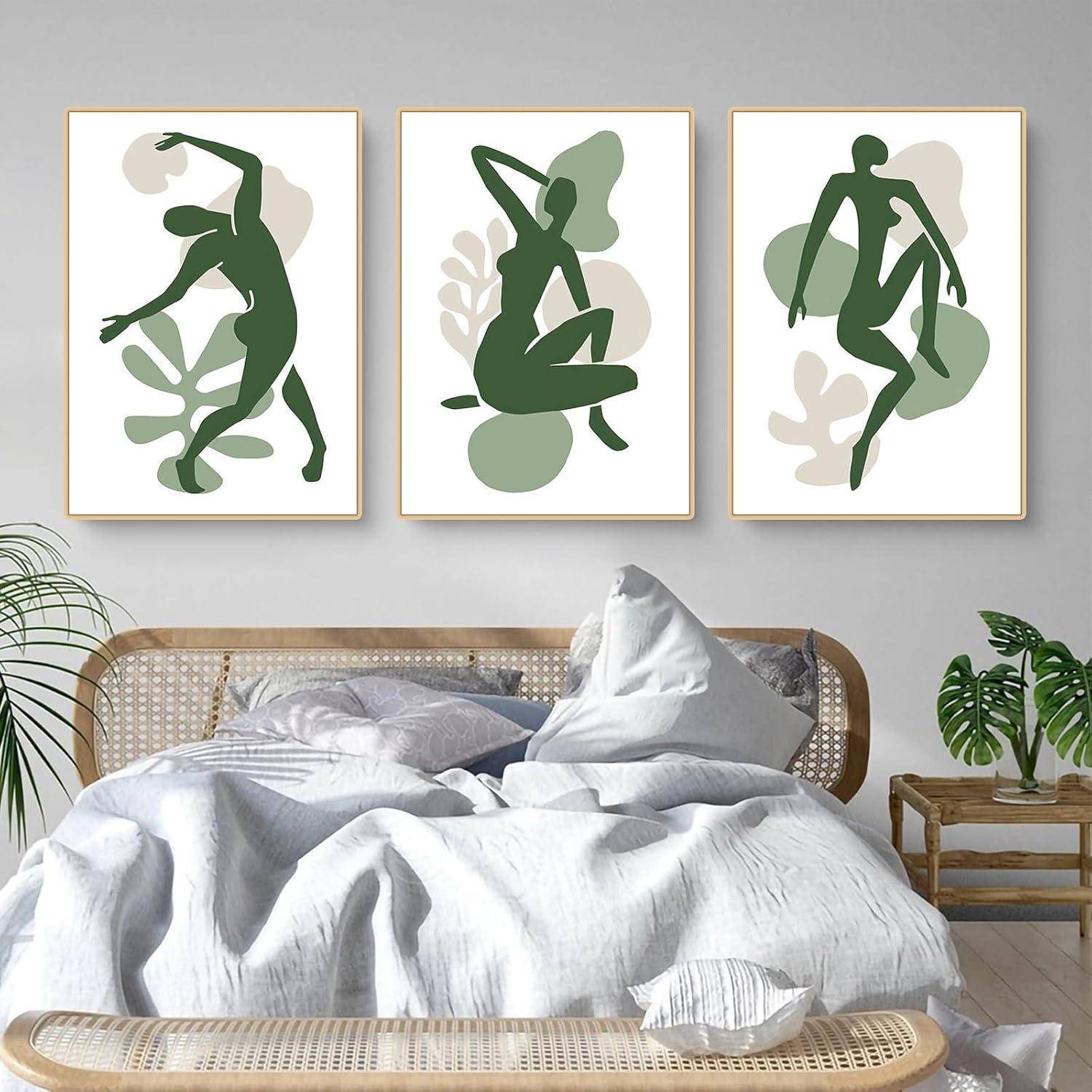 Drei abstrakte Silhouettenkunstwerke von tanzenden Figuren in verschiedenen Posen werden über einem hellgefärbten Bett mit grünen Pflanzen in der Nähe ausgestellt.