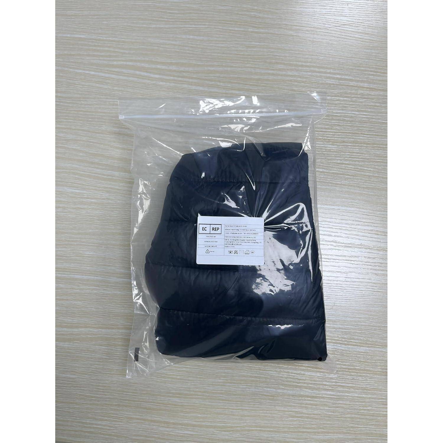 Eine sorgfältig gefaltete schwarze Daunenjacke ist in einem transparenten Plastikbeutel versiegelt, der auf einer hellen Holzoberfläche ruht.