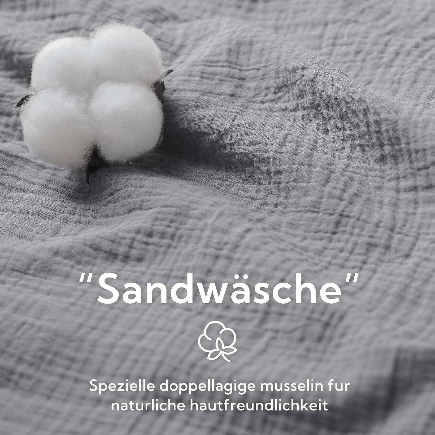 Ein Stück Baumwolle ruht auf strukturiertem grauen Stoff. Der Text darunter liest sich „Sandwäsche