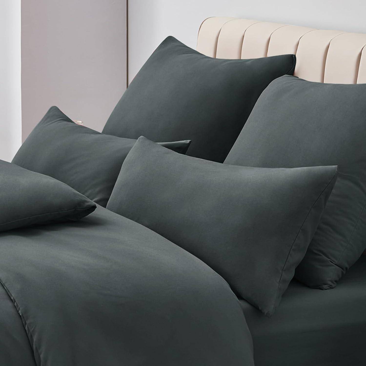 Ein ordentlich gemachtes Bett mit dunkelgrauen Kissen und Bettdecke vor einem hellen Kopfteil und einer hellen Wand, was einen gemütlichen und modernen Look schafft.