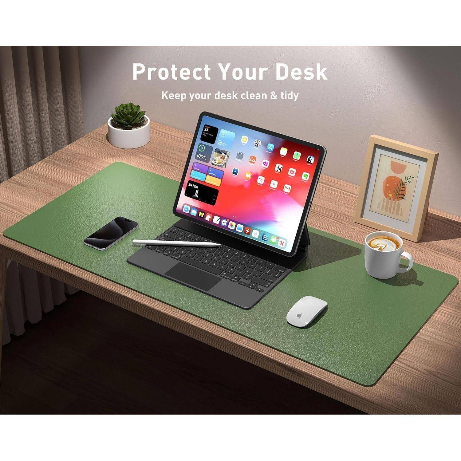 Ein Tablet in einem Tastaturgehäuse, ein Smartphone, eine Maus, eine Kaffeetasse und eine Pflanze stehen auf einem aufgeräumten Schreibtisch mit einer grünen Unterlage. Wandkunst im Hintergrund.