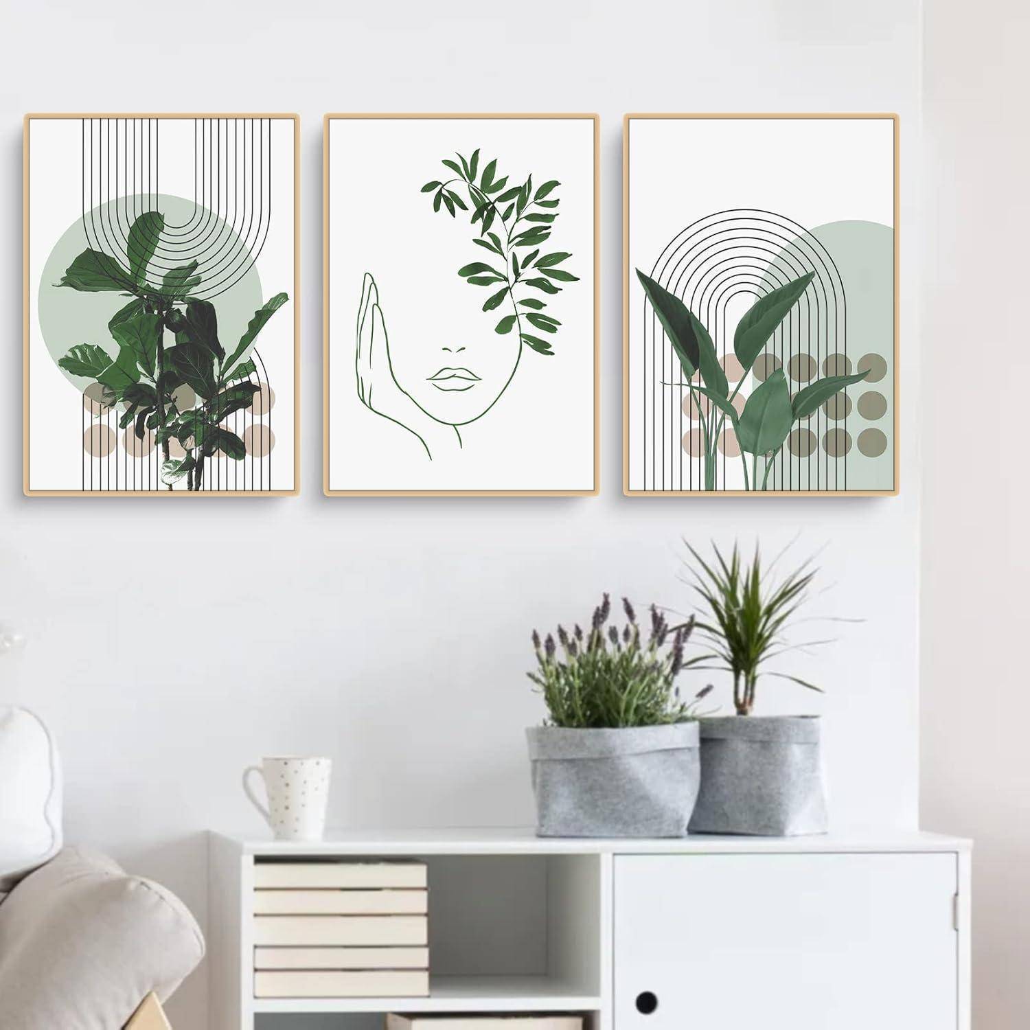 Drei gerahmte abstrakte botanische Kunstwerke an einer Wand. Die Kunst zeigt grüne Blätter, geometrische Formen und eine Gesichtsumrisse. Darunter befinden sich Pflanzen und Bücher.