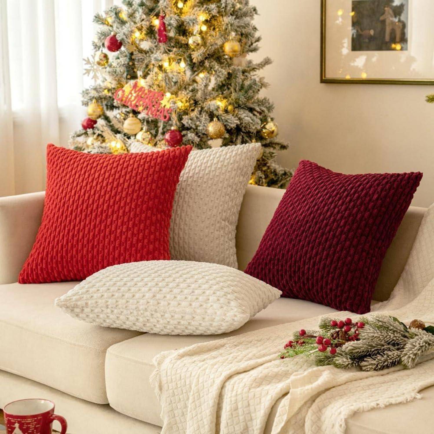 Ein gemütliches Wohnzimmer mit einem beigen Sofa, geschmückt mit roten und weißen gestrickten Kissen, vor einem geschmückten Weihnachtsbaum mit Lichtern und Christbaumschmuck.