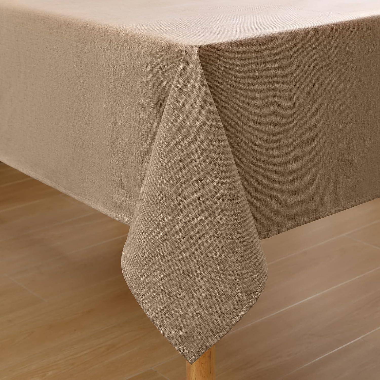 Ein beige Tischdecke drapiert sich glatt über einen Holztisch in einem Raum mit Holzfußboden und verleiht der Umgebung einen warmen, neutralen Ton.