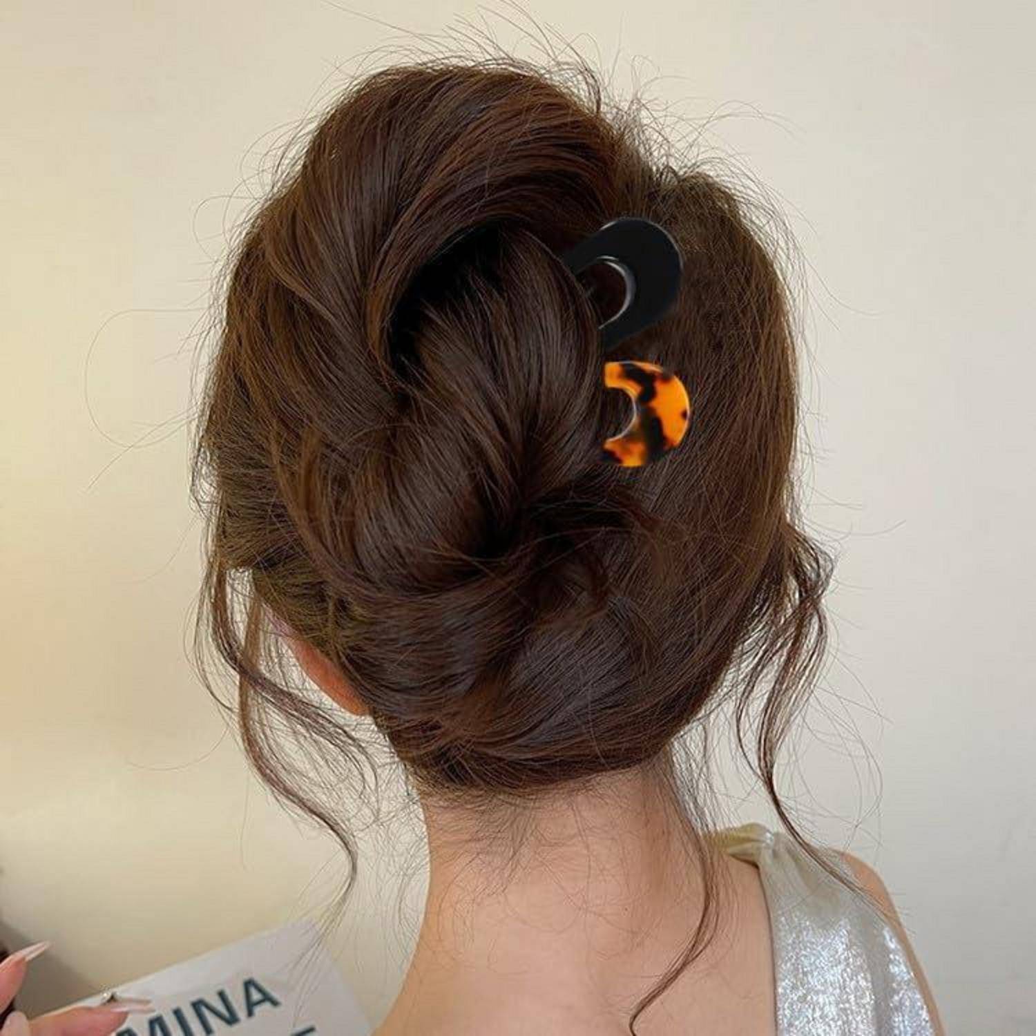 Eine Frau mit langen braunen Haaren, die zu einer eleganten Hochsteckfrisur gebunden sind und mit einer Schildpatt-Haarspange befestigt werden, ist von hinten zu sehen.