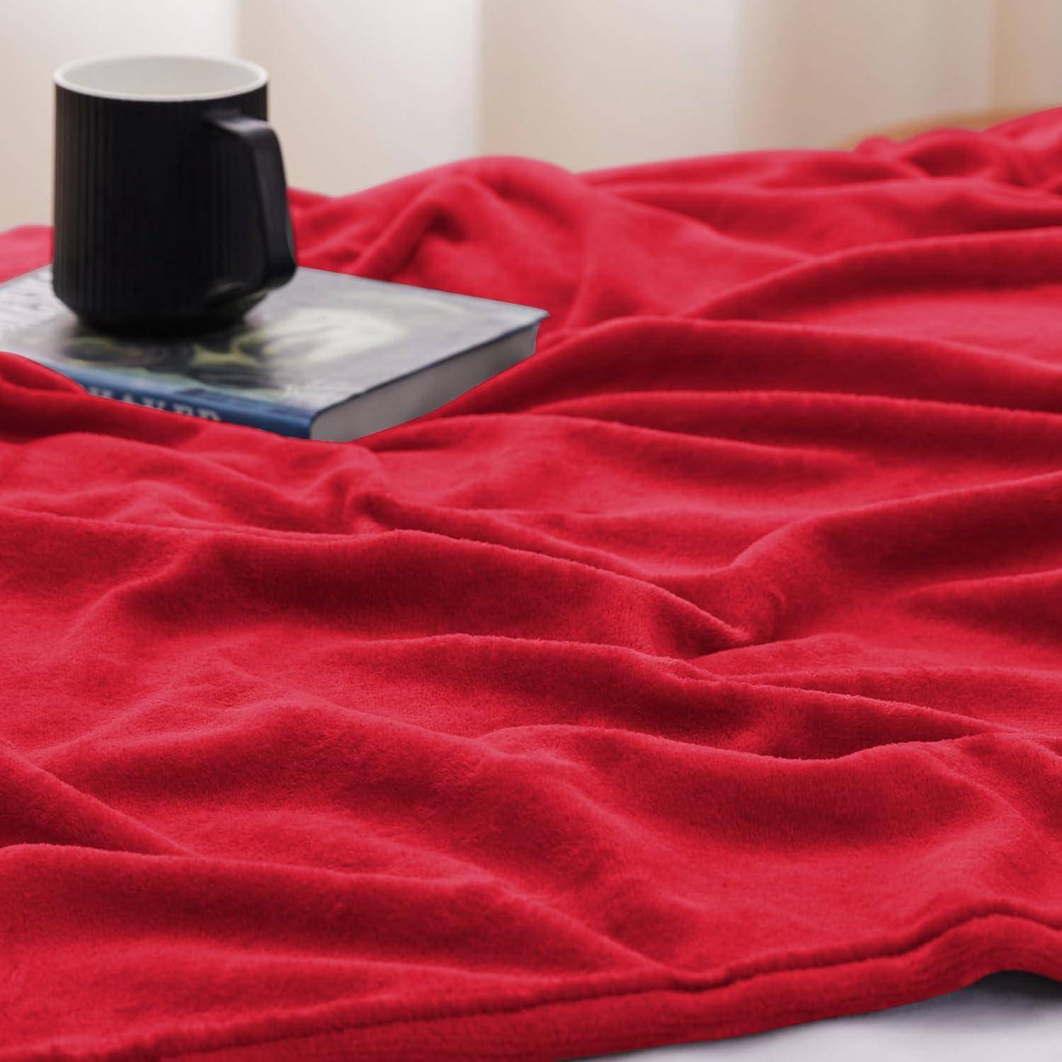 Eine rote Decke liegt auf einer Oberfläche mit einer schwarzen Kaffeetasse und einem geschlossenen Buch darauf. Die Szene ist gemütlich und einladend.