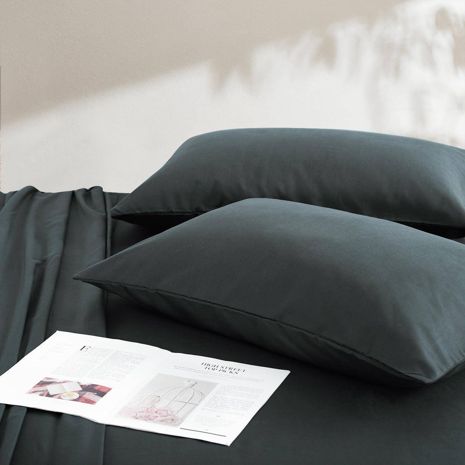 Ein Bett mit dunkelgrauen Kissen und Bettwäsche, ein aufgeschlagenes Buch mit Illustrationen liegt darauf und deutet auf einen gemütlichen Lesebereich hin.