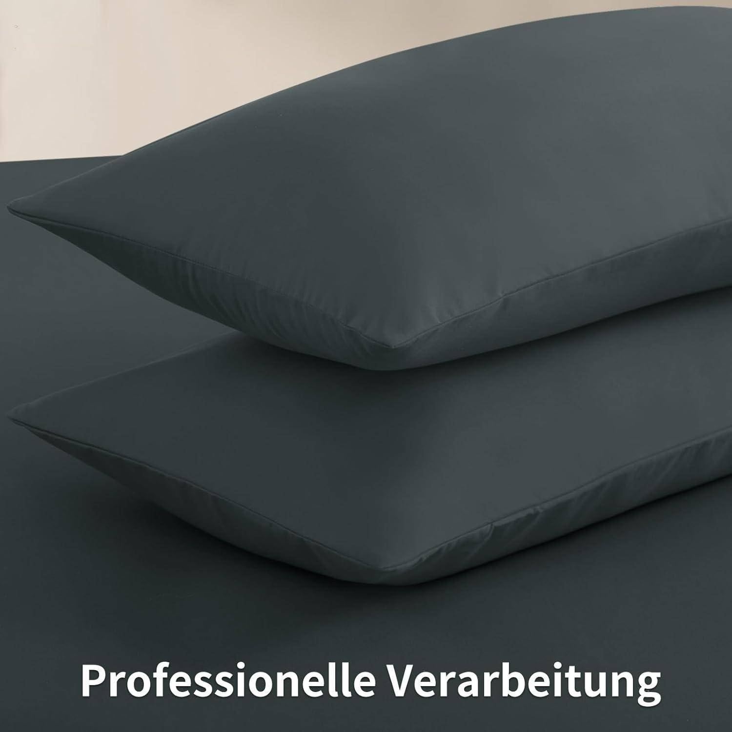 Zwei übereinander gestapelte dunkelgraue Kissen auf einer grauen Oberfläche. Text darunter liest sich 'Professionelle Verarbeitung'.