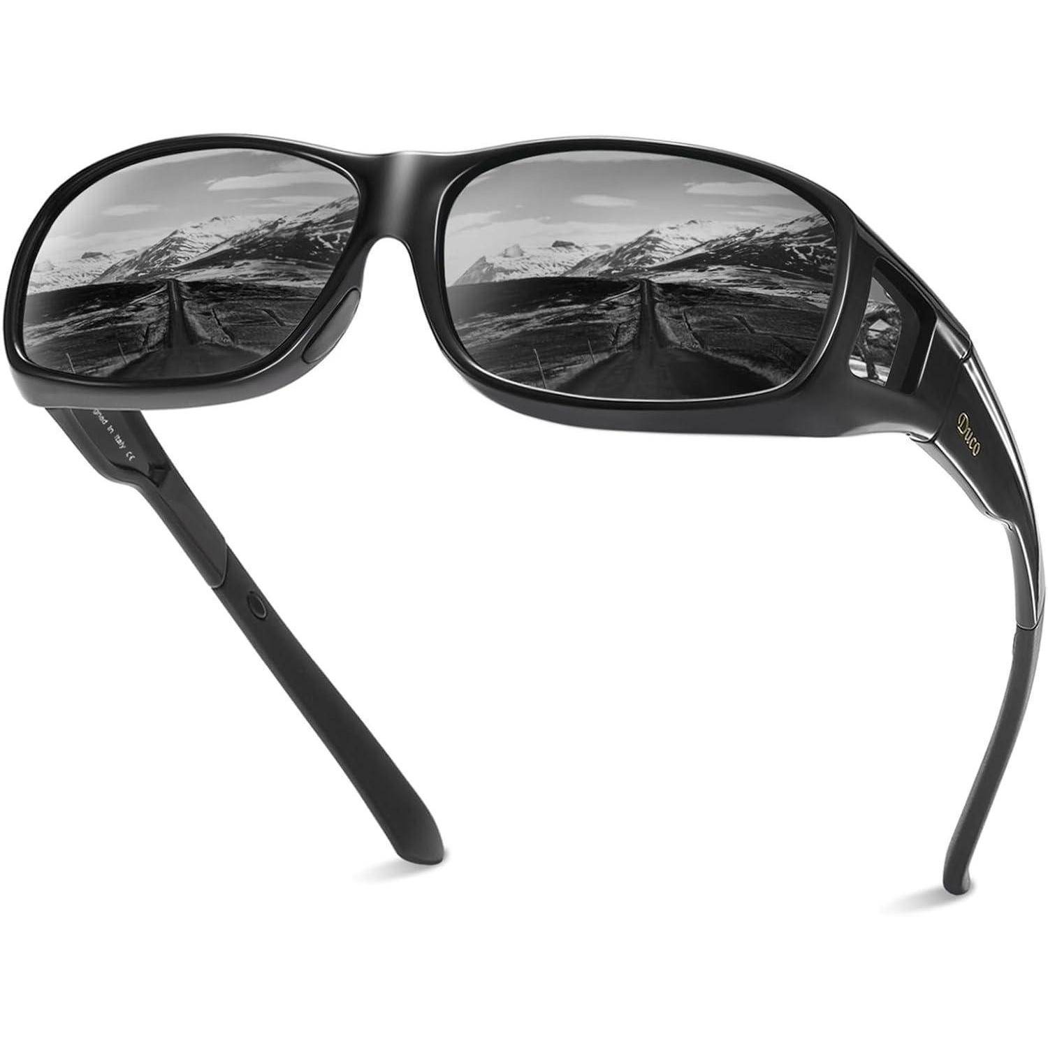 Schwarze Sonnenbrille mit Landschaftsreflexion auf den Gläsern, die eine Straße zeigt, die auf schneebedeckte Berge zuführt, unter einem bewölkten Himmel.
