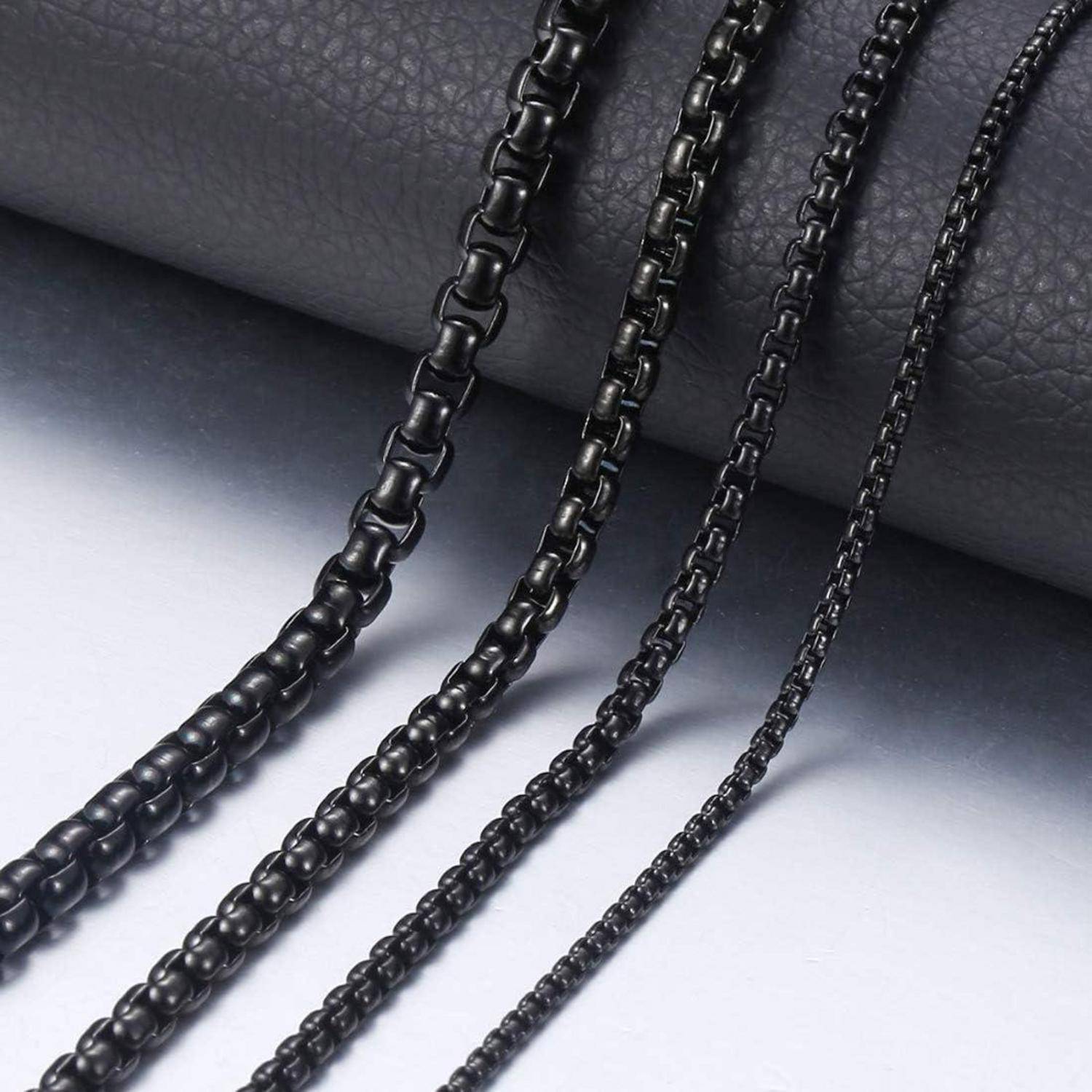 Drei schwarze Metallketten unterschiedlicher Stärke, die auf einer dunklen Oberfläche ausgelegt sind und deren Textur und Reflektionseigenschaften hervorgehoben werden.
