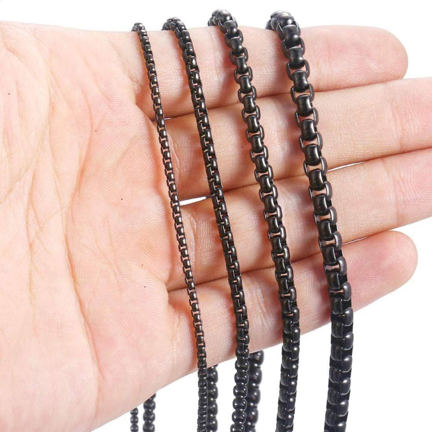 Eine Hand, die mehrere metallische schwarze Ketten unterschiedlicher Größen hält, vor einem schlichten weißen Hintergrund dargestellt.