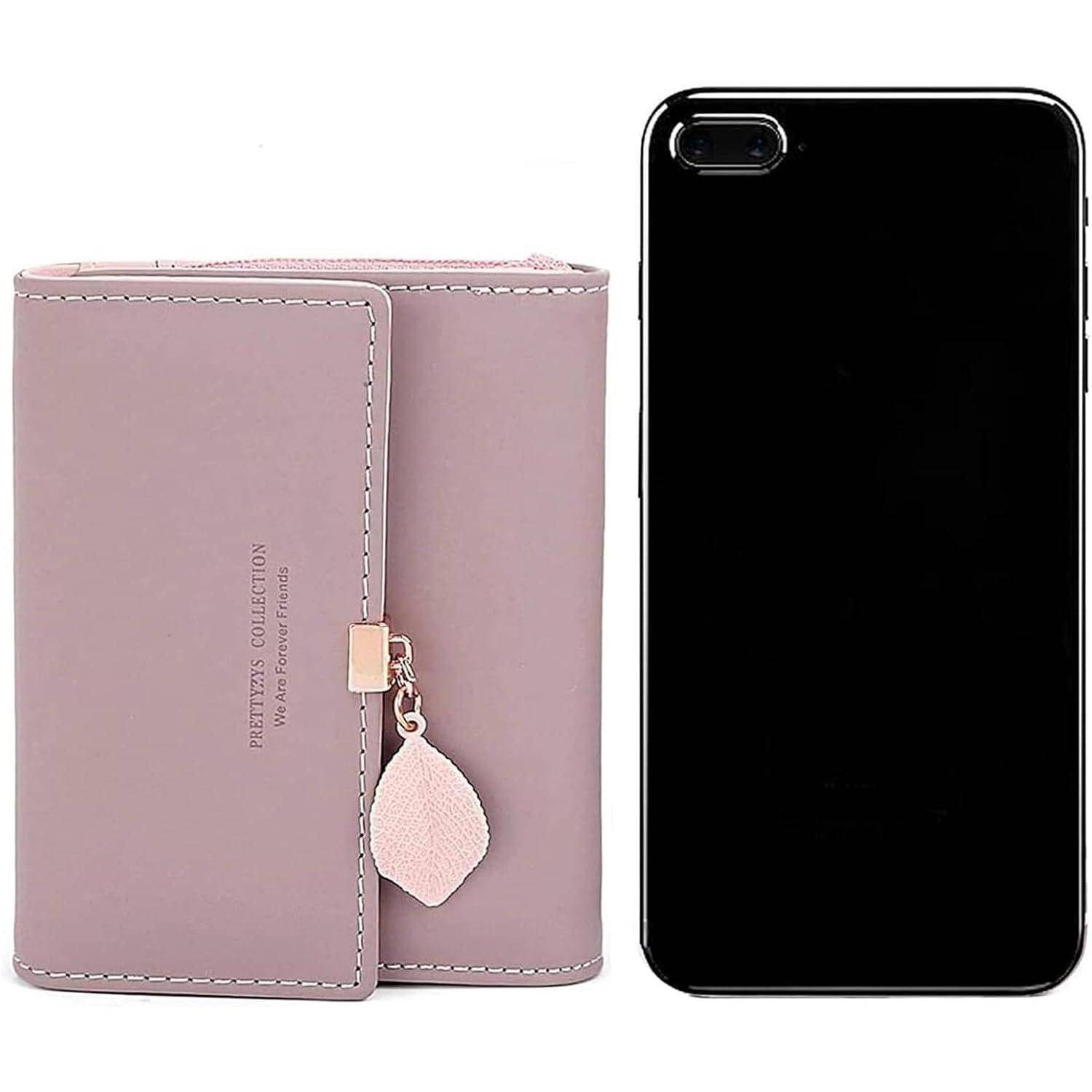 Ein rosa Portemonnaie mit einem blattförmigen Anhänger liegt neben einem schwarzen Smartphone. Das Portemonnaie ist geschlossen und steht aufrecht.