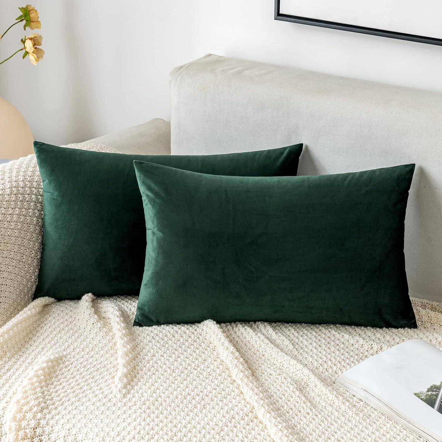 Zwei dunkelgrüne Samtdecken liegen auf einer hellbeigen gestrickten Decke, die einen cremefarbenen Sofa in einem modernen, minimalistischen Raum bedeckt.